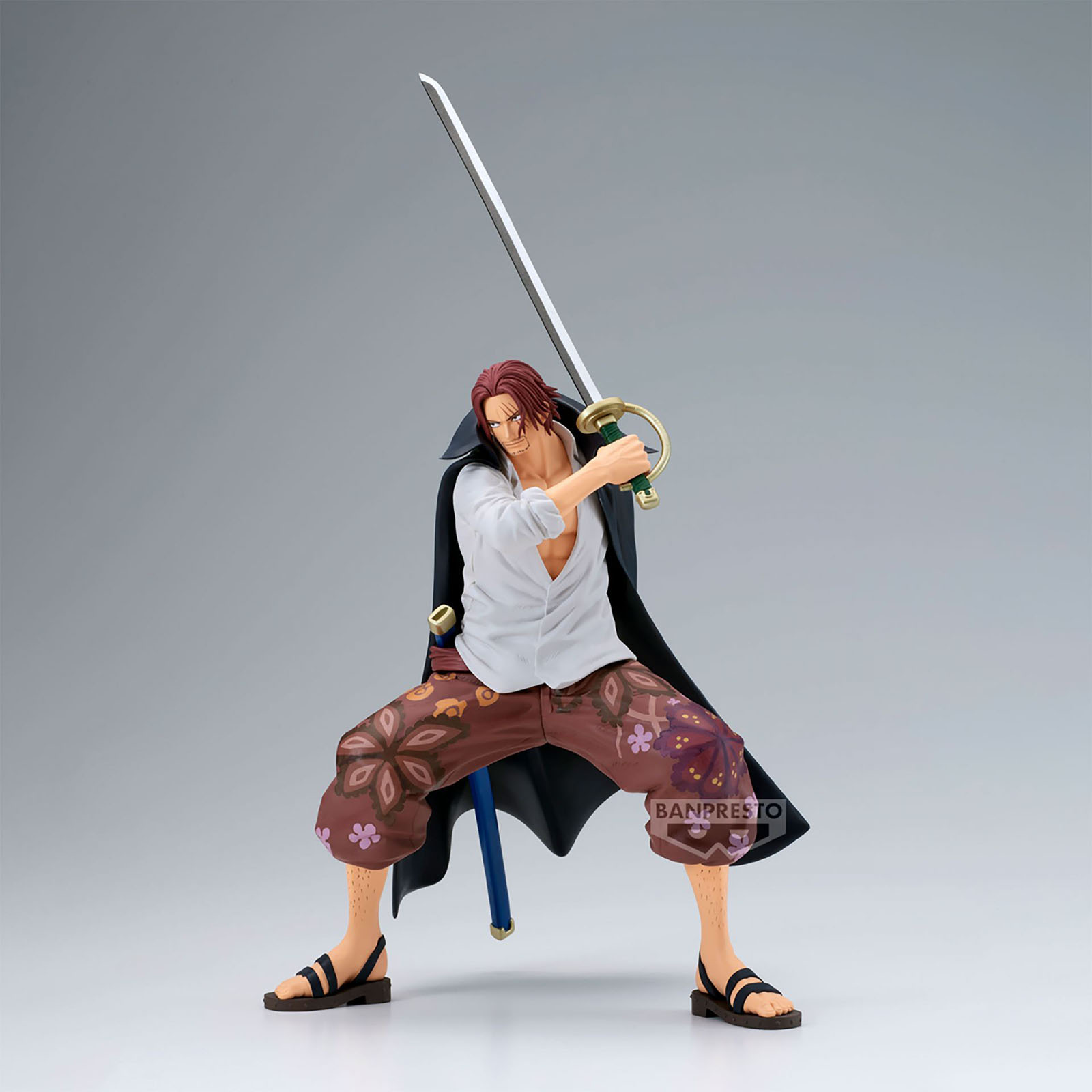 Eine Shanks-Figur mit Schwert. Er trägt ein weißes Hemd, braune Hosen mit Blumen, einen schwarzen Umhang und Sandalen. Grauer Hintergrund.