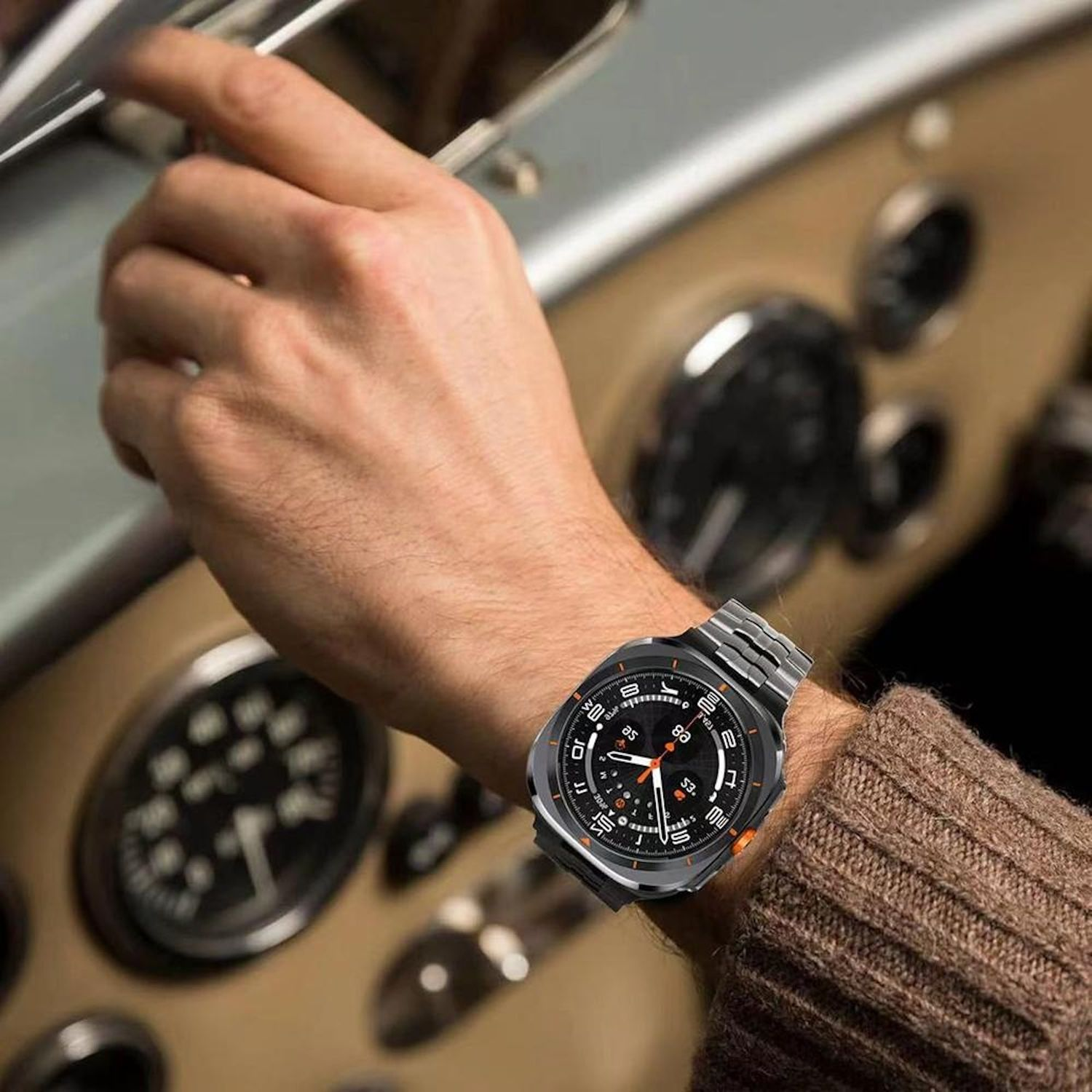 Ein Mann im Auto trägt eine Uhr. Die Uhr hat ein schwarzes Zifferblatt und orangefarbene Akzente. Das Armaturenbrett des Autos ist sichtbar.