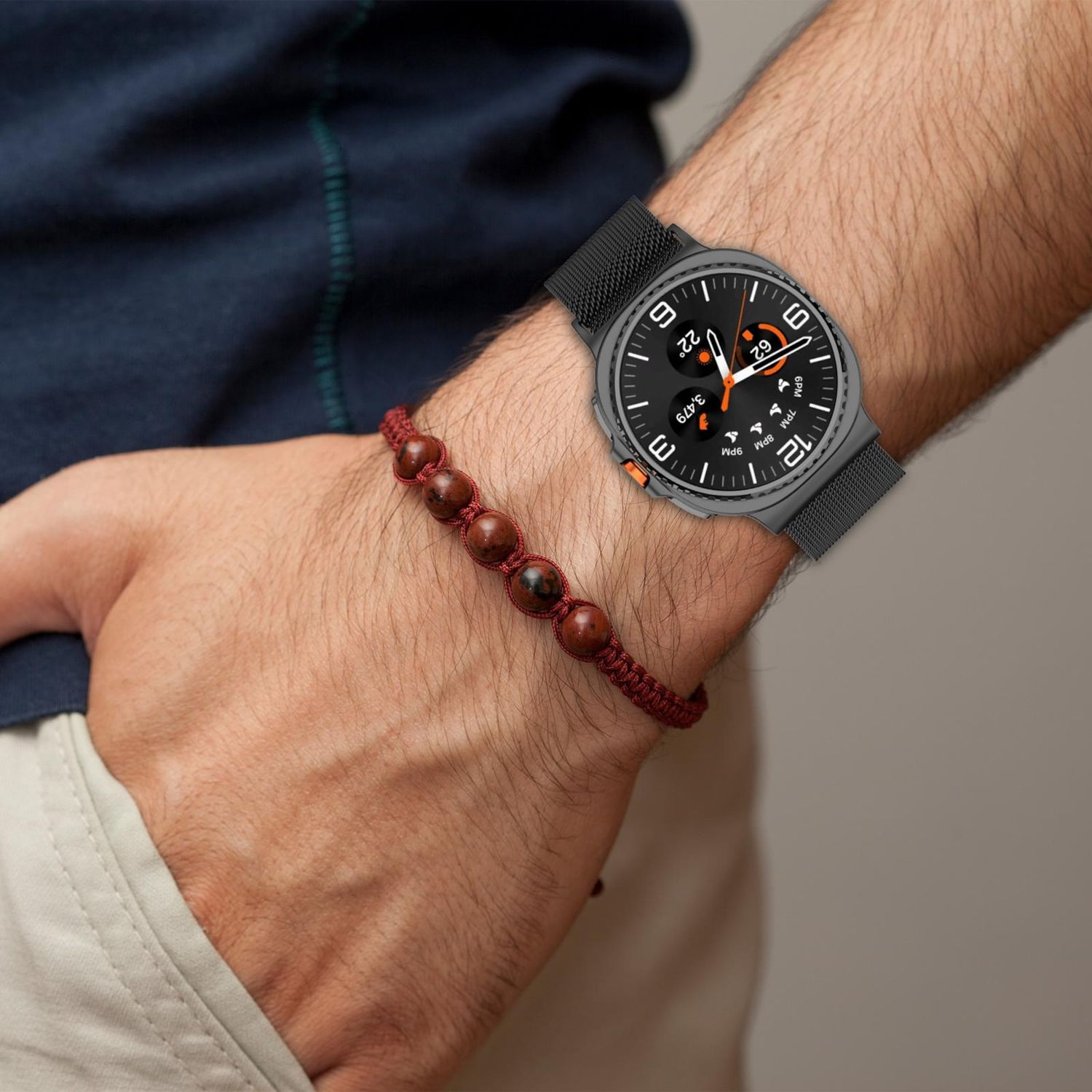 Das Handgelenk einer Person mit einer Smartwatch und einem Perlenarmband. Die Uhr zeigt Datum und Uhrzeit an. Das Armband hat rote Perlen.