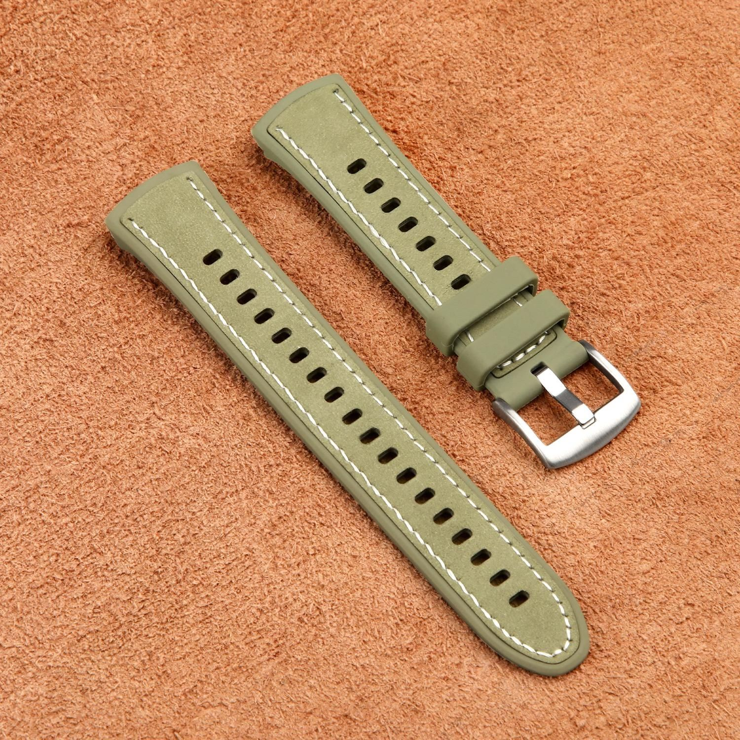 Zwei olivgrüne Uhrenarmbänder mit weißen Nähten und silberner Schnalle liegen auf einer strukturierten braunen Oberfläche.