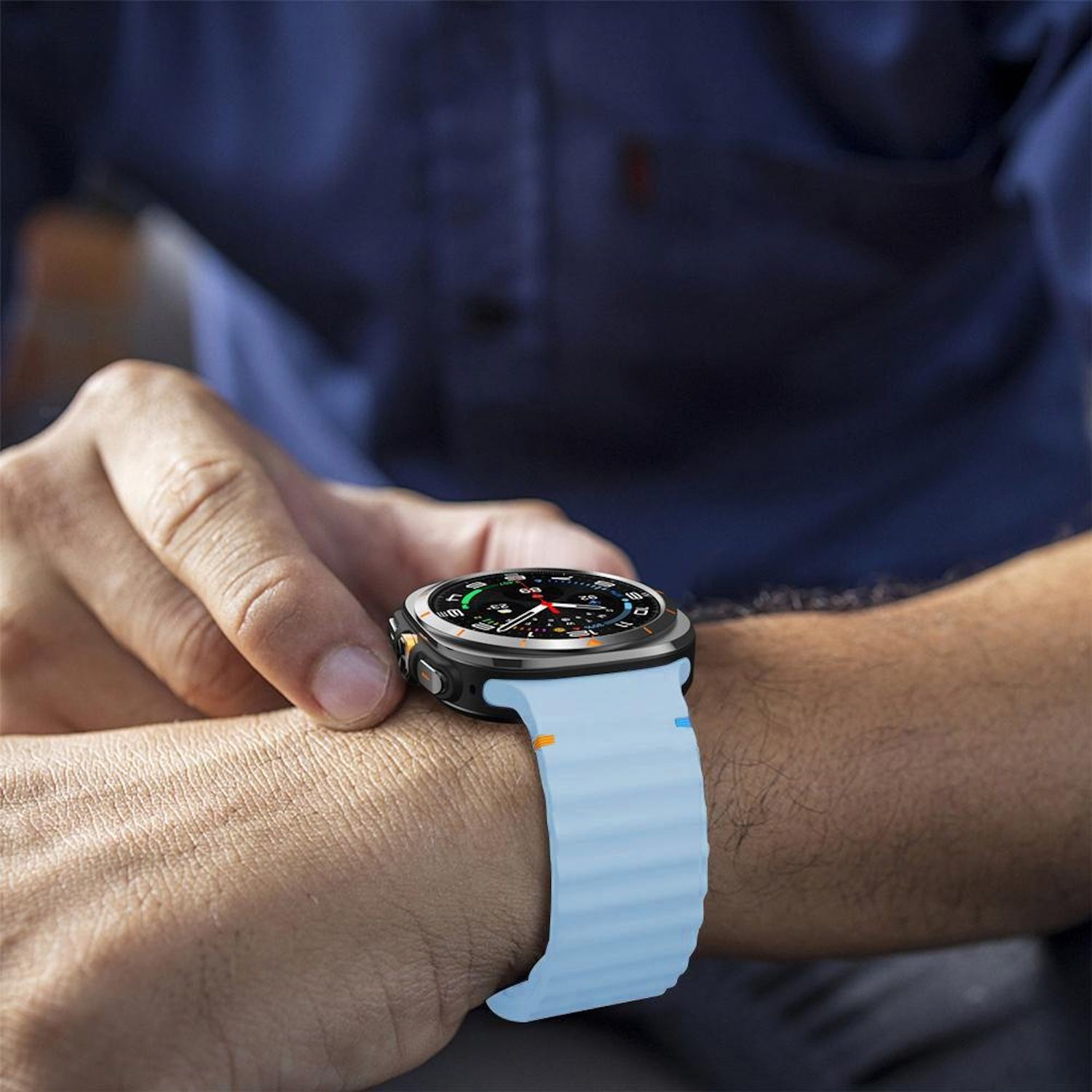Handgelenk einer Person mit einer Smartwatch. Die Uhr hat eine schwarze Lünette und ein hellblaues Armband. Die Hand berührt die Uhr.