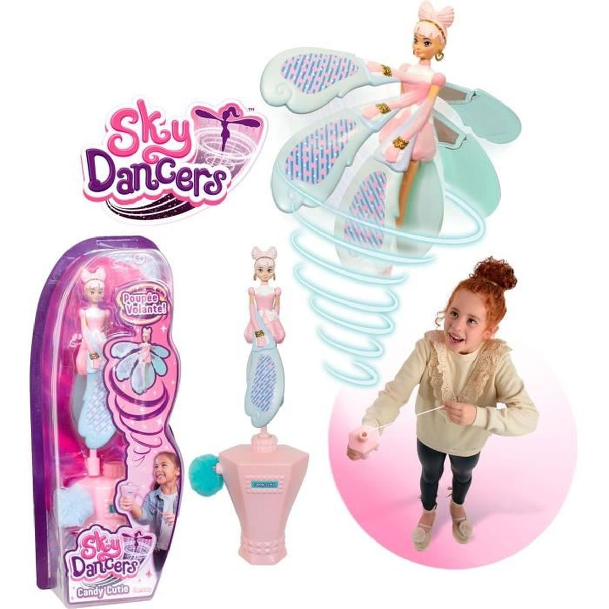 Ein Mädchen mit roten Haaren spielt mit einem Sky Dancers-Spielzeug. Das Spielzeug ist eine Puppe mit Flügeln. Eine rosa-blaue Box mit dem Spielzeug ist ebenfalls im Bild.