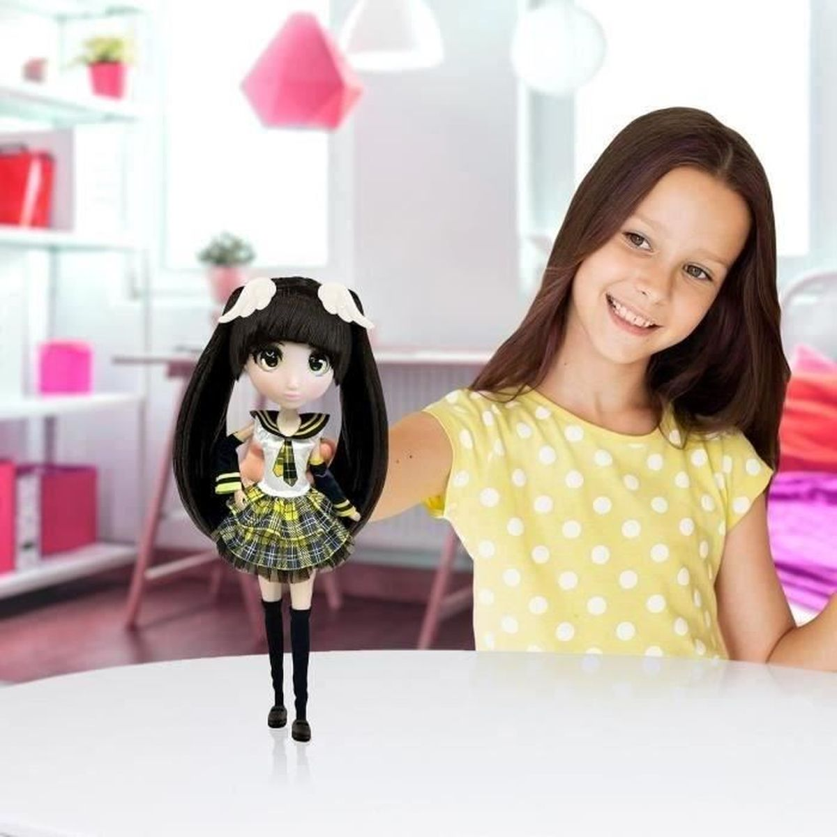 Ein Mädchen lächelt und hält eine Puppe. Die Puppe hat langes schwarzes Haar und ein Outfit im Matrosenstil. Das Mädchen trägt ein gelbes Polka-Dot-Shirt.
