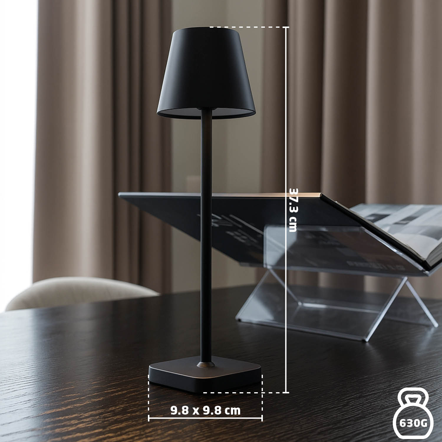 Een zwarte lamp op een houten tafel, een boekenhouder en bruine gordijnen op de achtergrond. De lamp is 37,3 cm hoog.