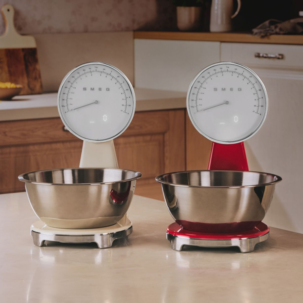 Dwie zabytkowe wagi kuchenne z miskami ze stali nierdzewnej. Jedna jest w kolorze kości słoniowej, druga czerwona. Obie pokazują zero na tarczach. Tło kuchni.
