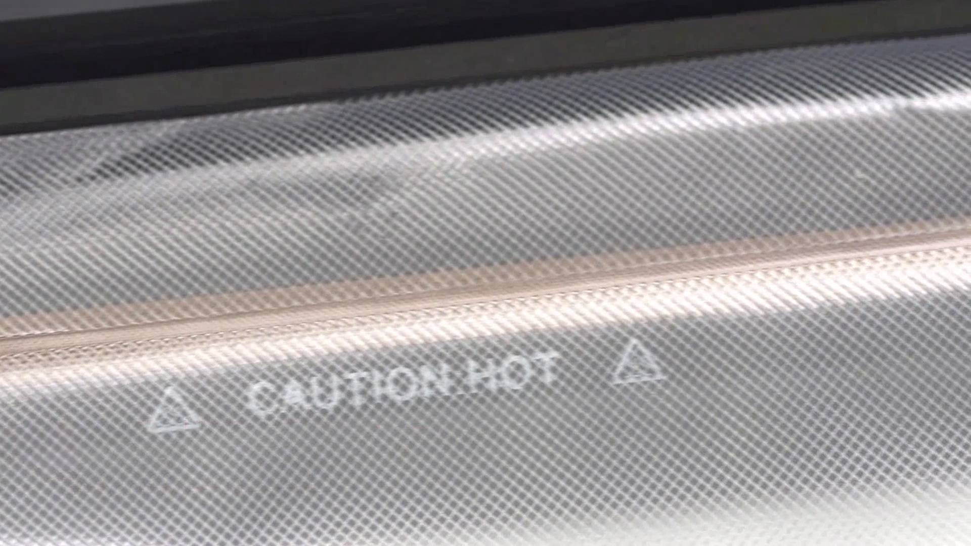 Zbliżenie powierzchni maszyny z wzorem siatki. Tekst brzmi 'CAUTION HOT' ze znakami ostrzegawczymi.