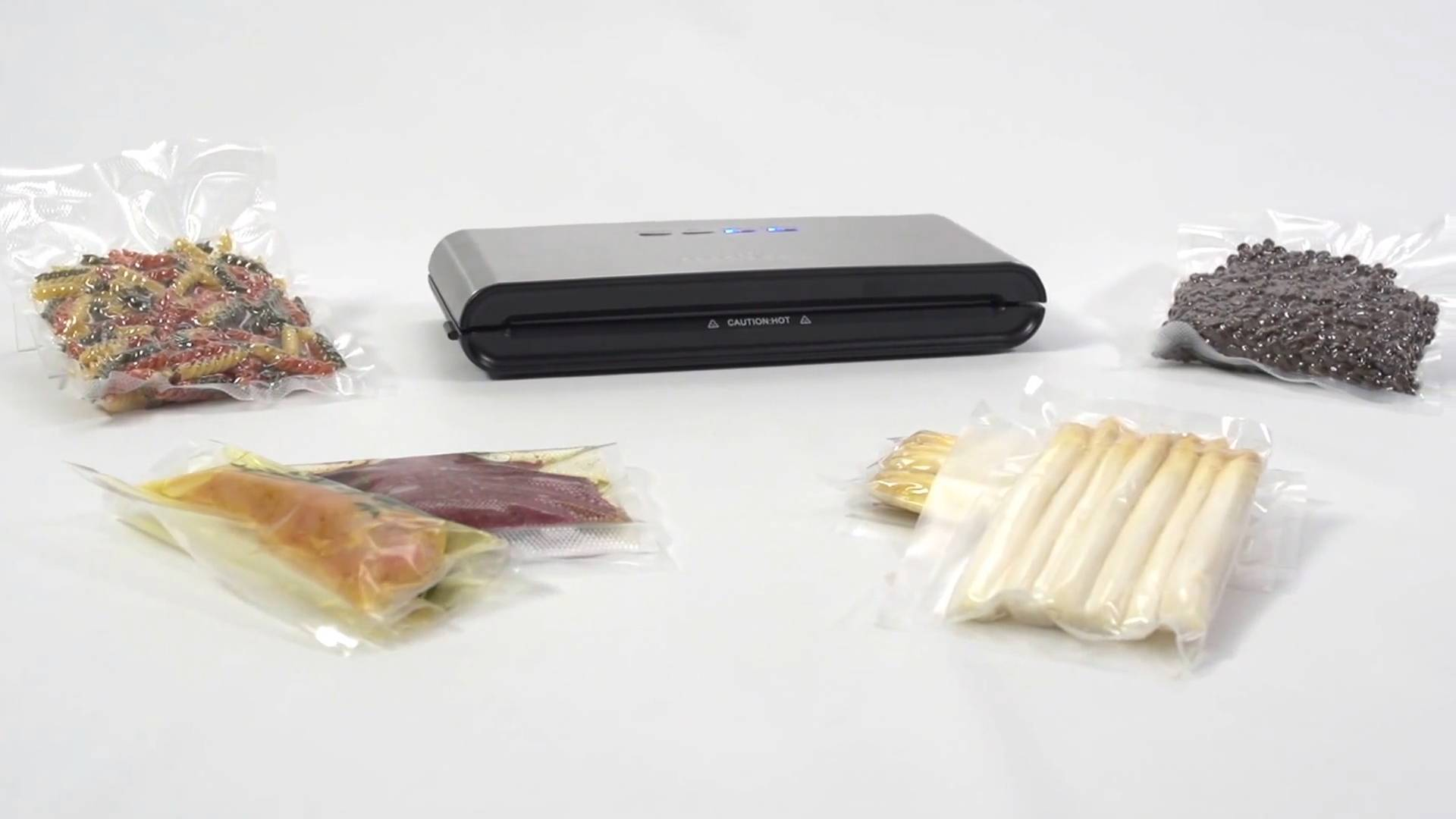 Zgrzewarka próżniowa z różnymi produktami spożywczymi zapakowanymi w plastikowe worki: makaron, fasola, szparagi i mięso. Wszystko na białej powierzchni.