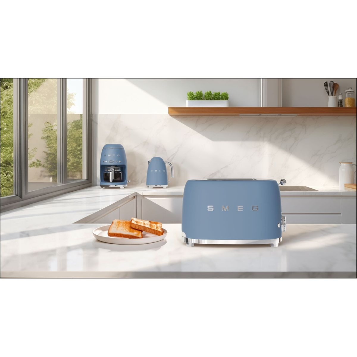 Ein blauer Smeg-Toaster, eine Kaffeemaschine und ein Wasserkocher auf einer Küchentheke. Zwei Toastscheiben auf einem Teller. Fenster und Pflanzen im Hintergrund.