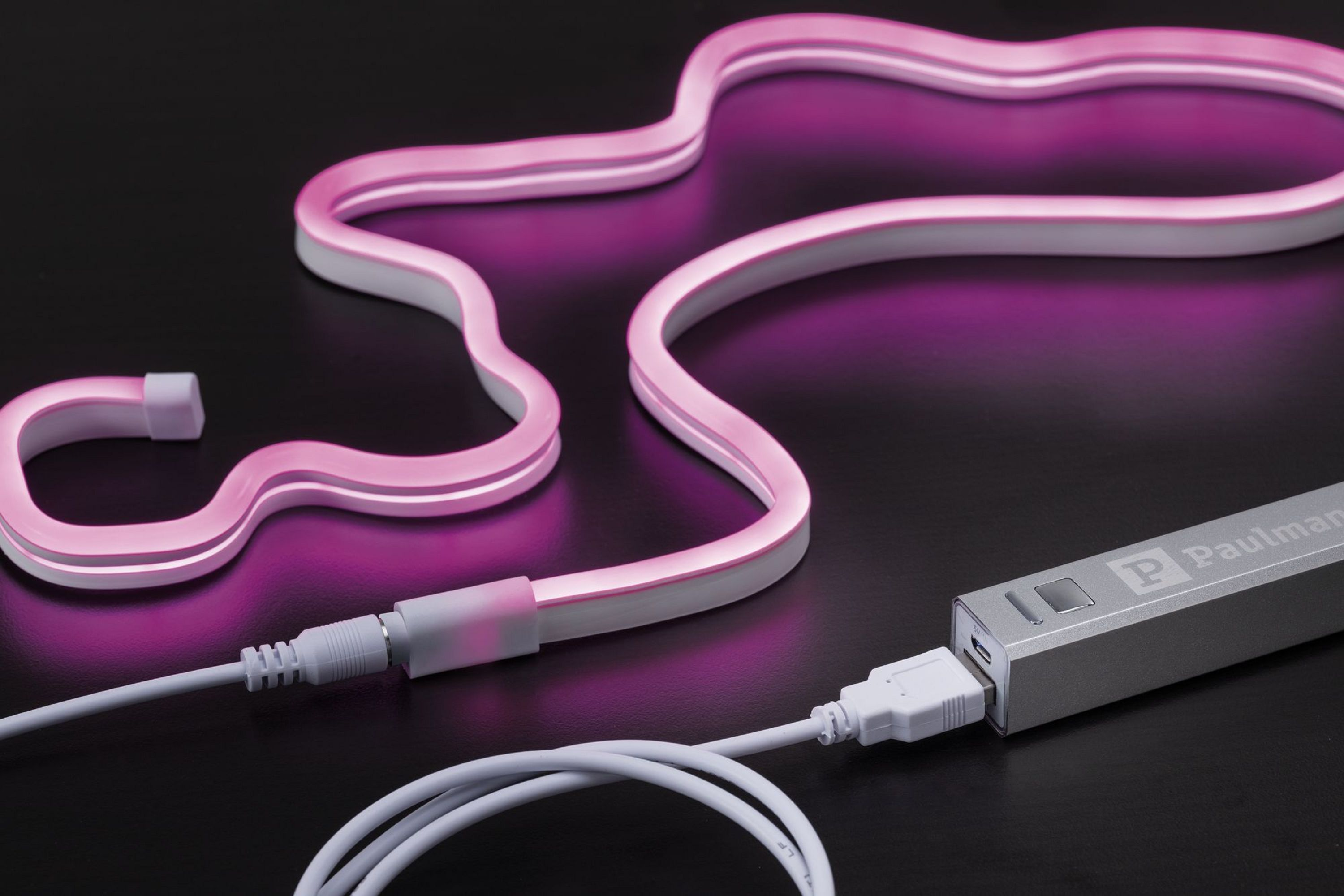 Różowe światło neonowe podłączone do srebrnego power banku za pomocą kabla USB, na czarnej powierzchni.