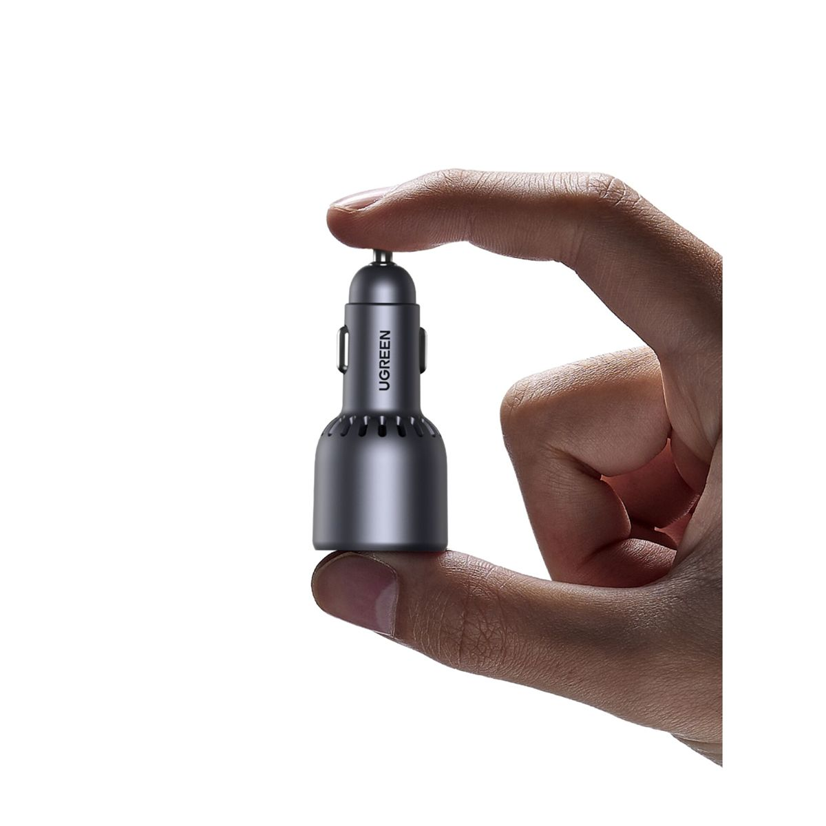 Ręka trzyma szarą ładowarkę samochodową UGREEN na białym tle. Ładowarka jest cylindryczna z teksturowaną podstawą.