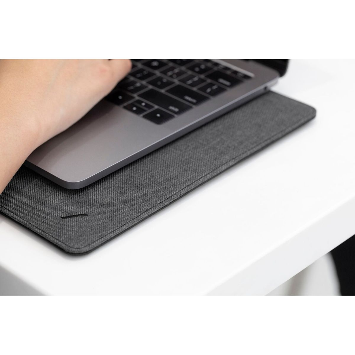 Una mano poggia su un laptop posizionato su un tappetino grigio. Il laptop è argentato e la scrivania è bianca. La scena è ben illuminata.