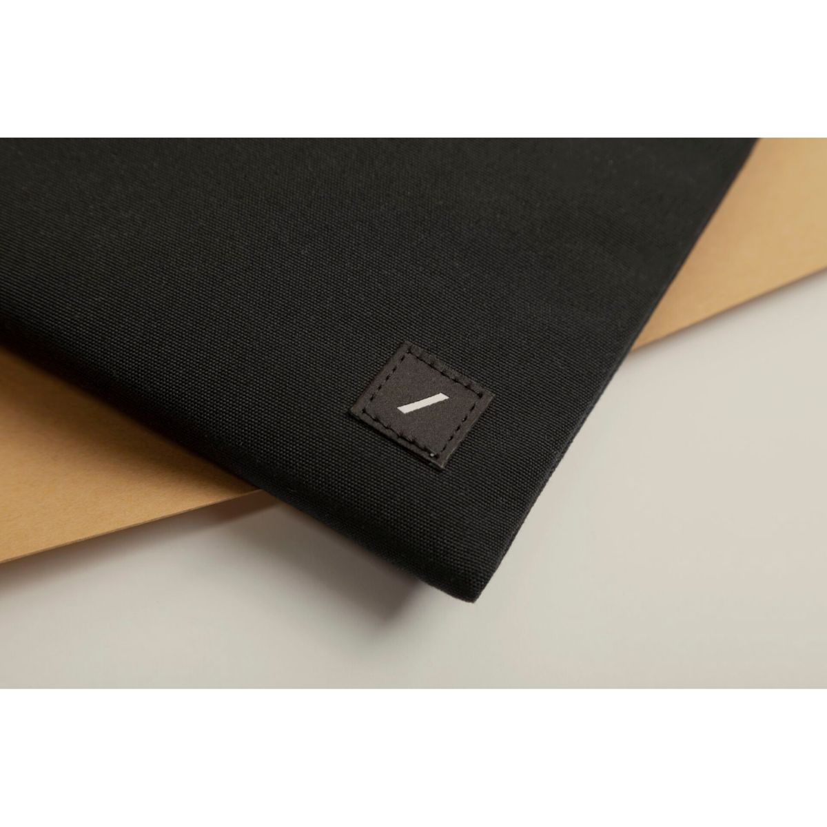 Gros plan sur une pochette en tissu noir avec un petit patch carré. Le patch a une ligne diagonale blanche. Le fond est beige et blanc.