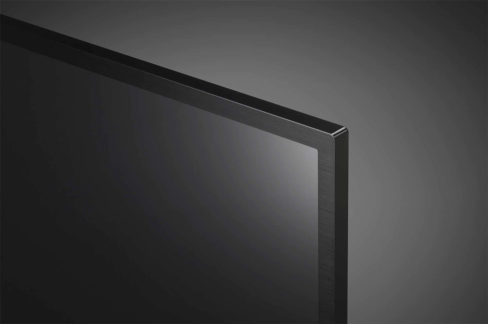 Zbliżenie rogu czarnego ekranu telewizora. Rama jest ciemnoszara. Tło jest rozmyte szare.