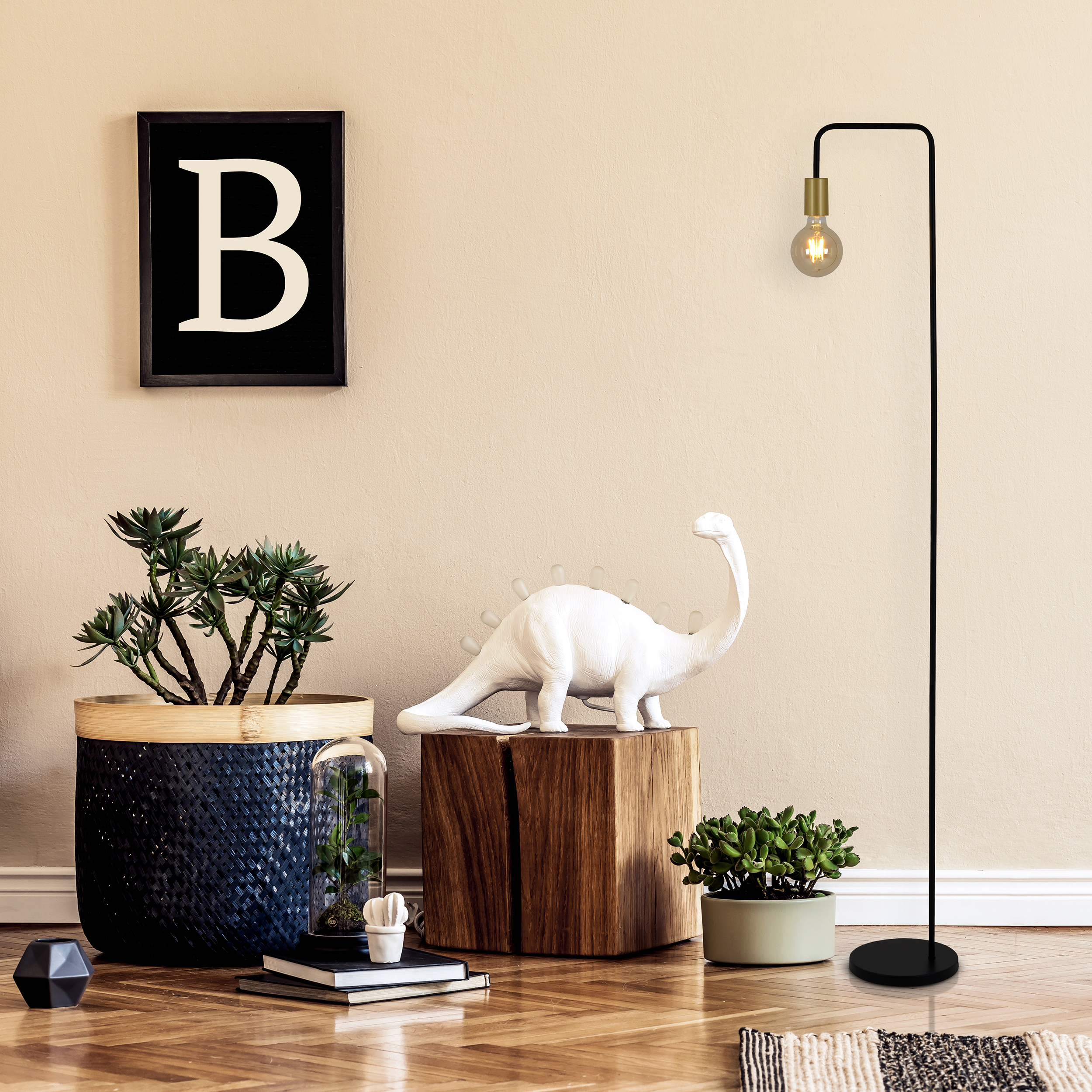 Ein Raum mit Pflanzen, einer Dinosaurierfigur, einer Stehlampe, einem gerahmten B und einem Holzboden.