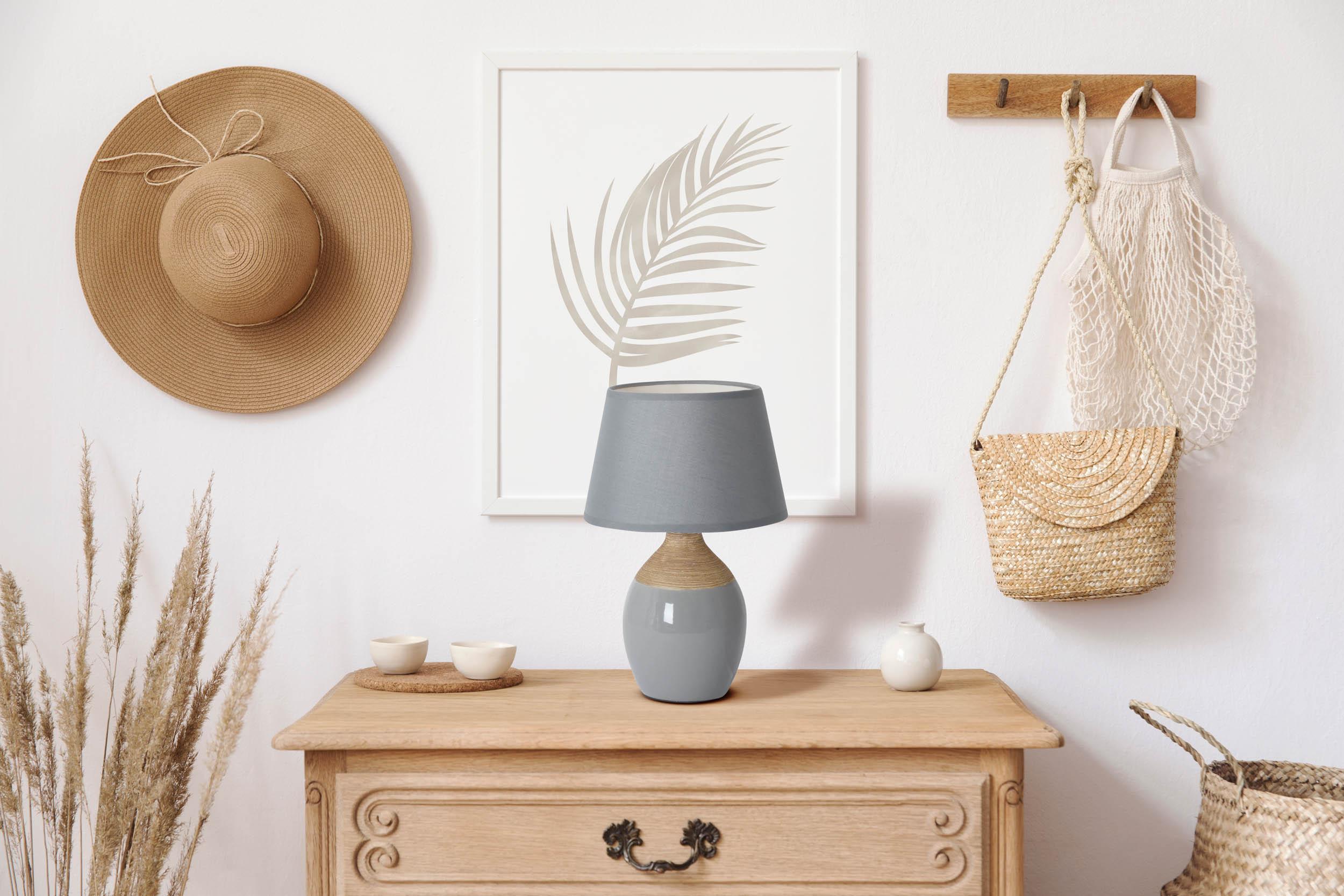 Ein Raum mit Hut, Lampe, Kunst, Tassen und einer gewebten Geldbörse auf einem Holztisch und einer Wand.