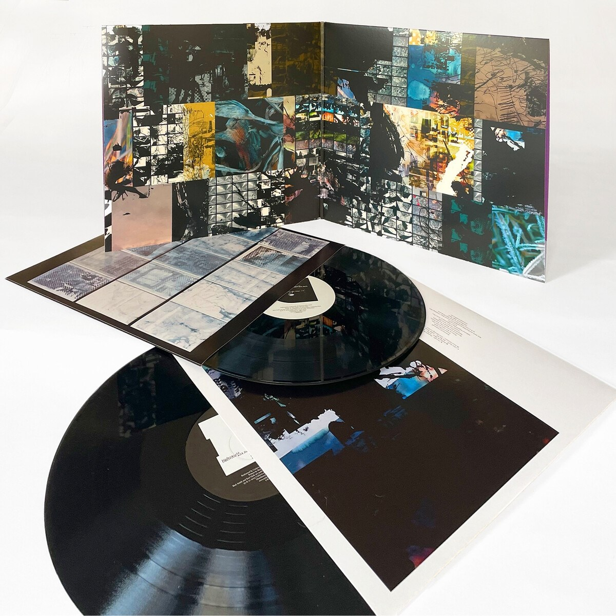 Due dischi in vinile con copertina dell'album, uno nella sua custodia. La copertina dell'album è astratta con colori scuri e forme geometriche.