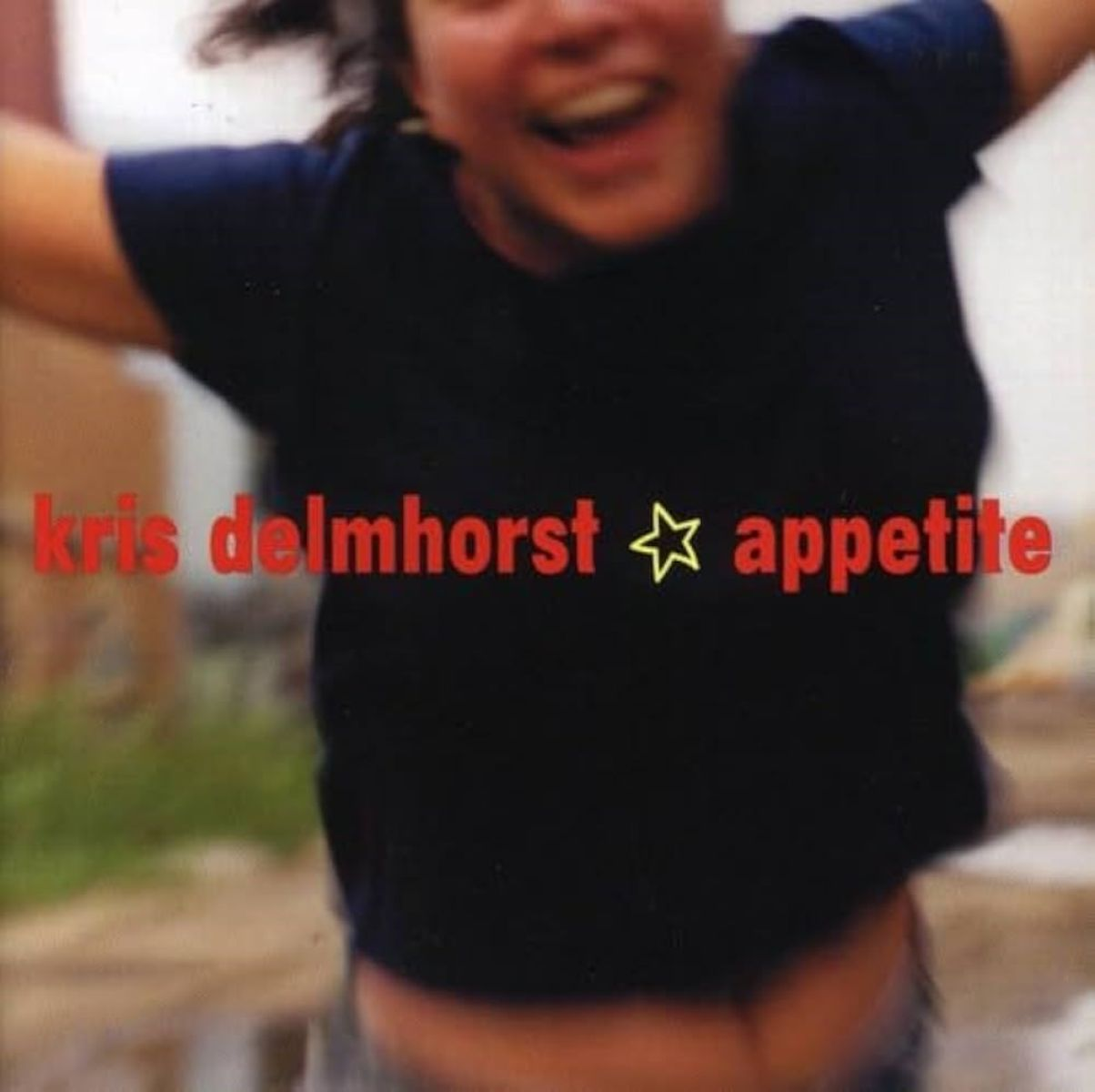 Albumhoes. Een vrouw in een zwart shirt lacht. Tekst: kris delmhorst appetite, met een ster symbool. Achtergrond is wazig.