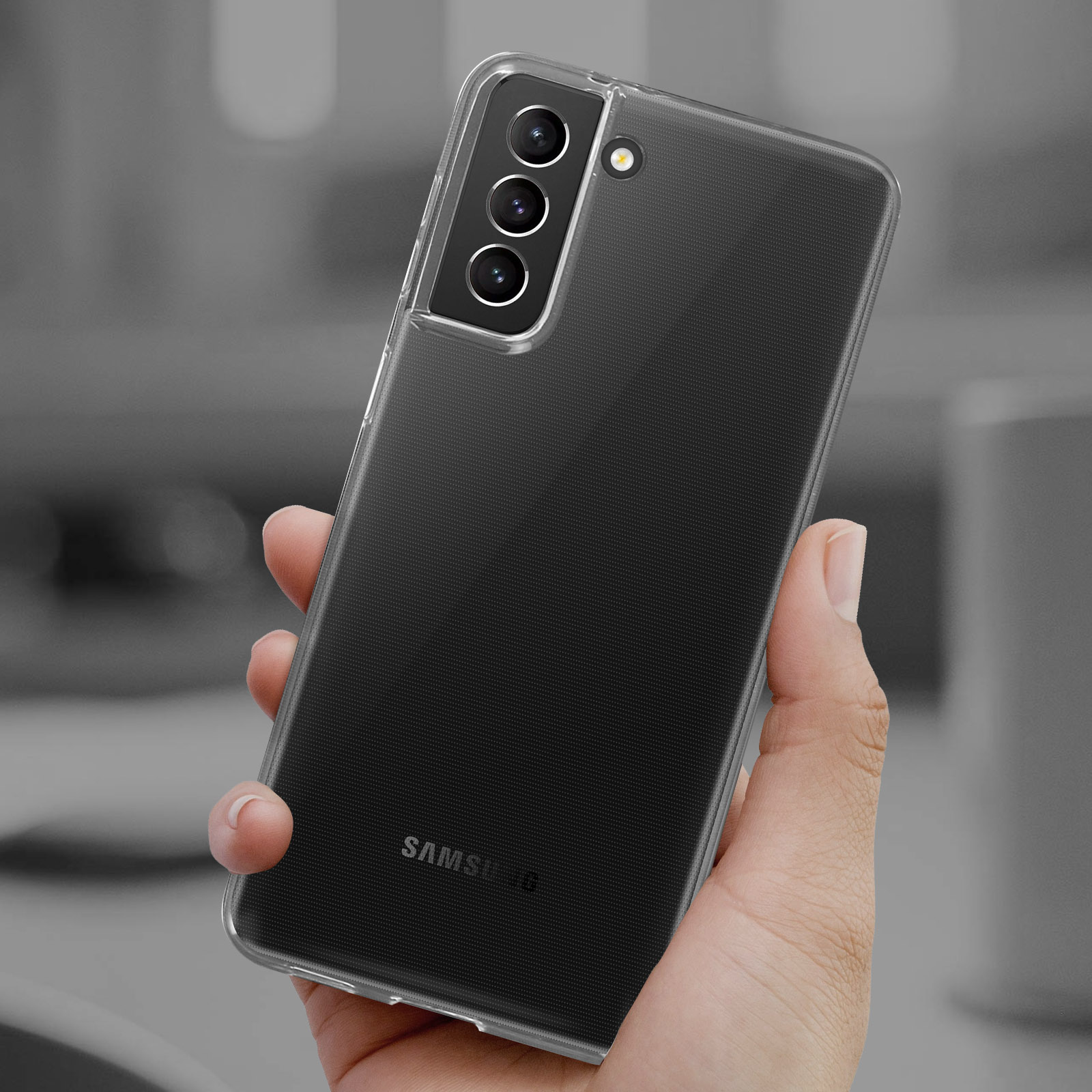 Hand hält eine transparente Handyhülle über einem schwarzen Telefon. Merkmale sind das Samsung-Logo und drei Kameralinsen.