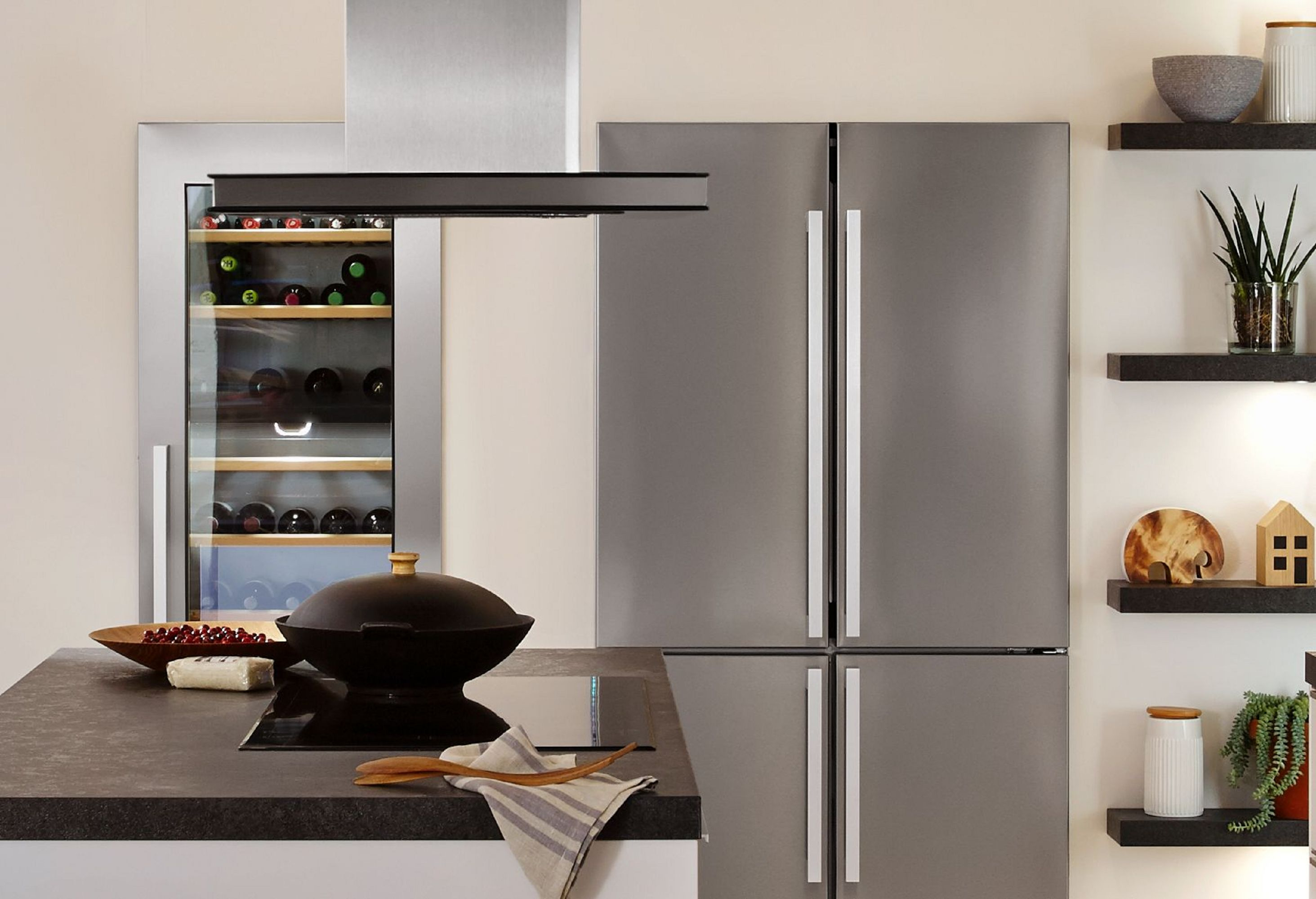 Nowoczesna kuchnia ze sprzętem ze stali nierdzewnej i ciemnymi blatami. Chłodziarka, lodówka i półki.