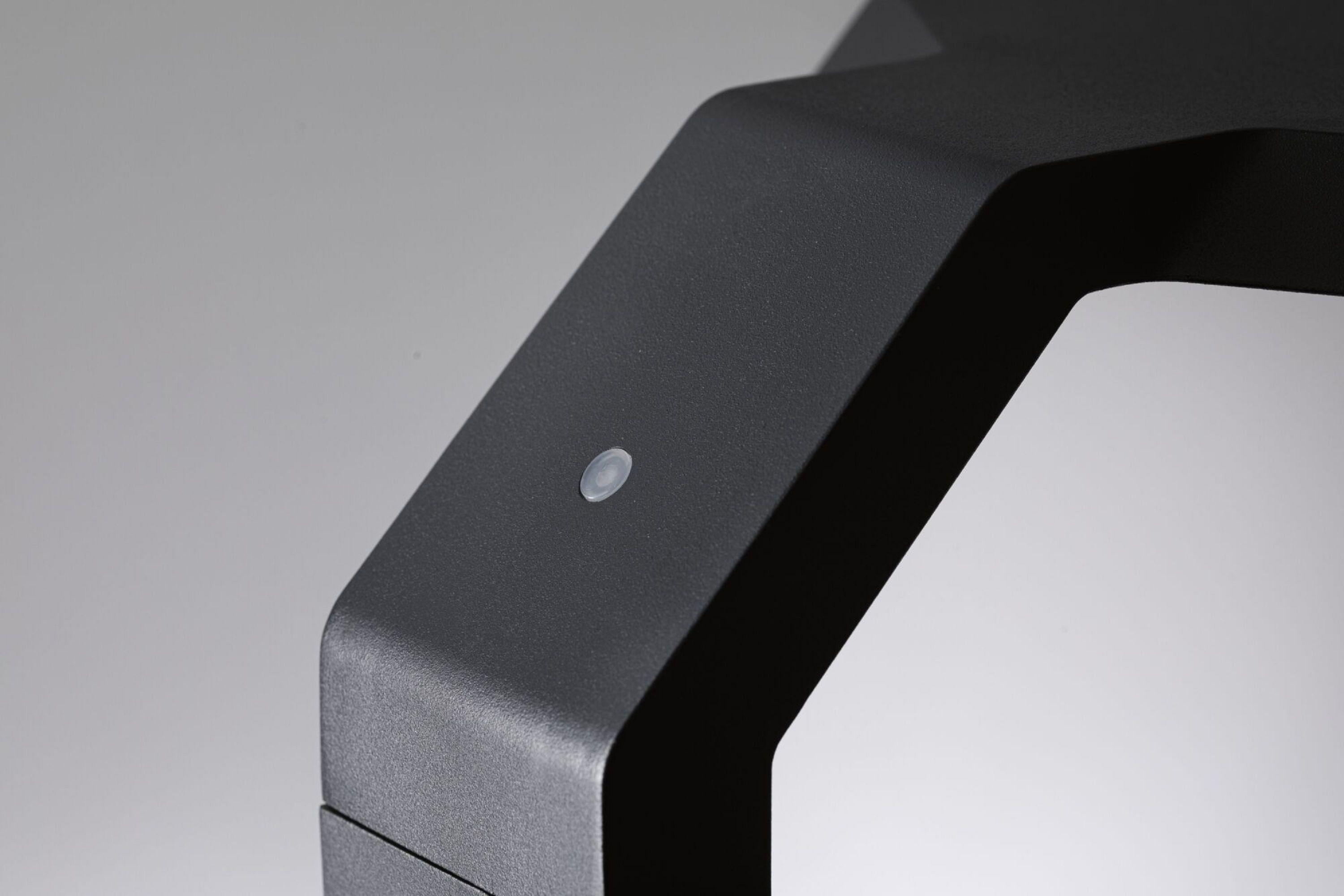 Zbliżenie rogu czarnego obiektu z małym, okrągłym, przezroczystym przyciskiem. Miękkie szare tło.