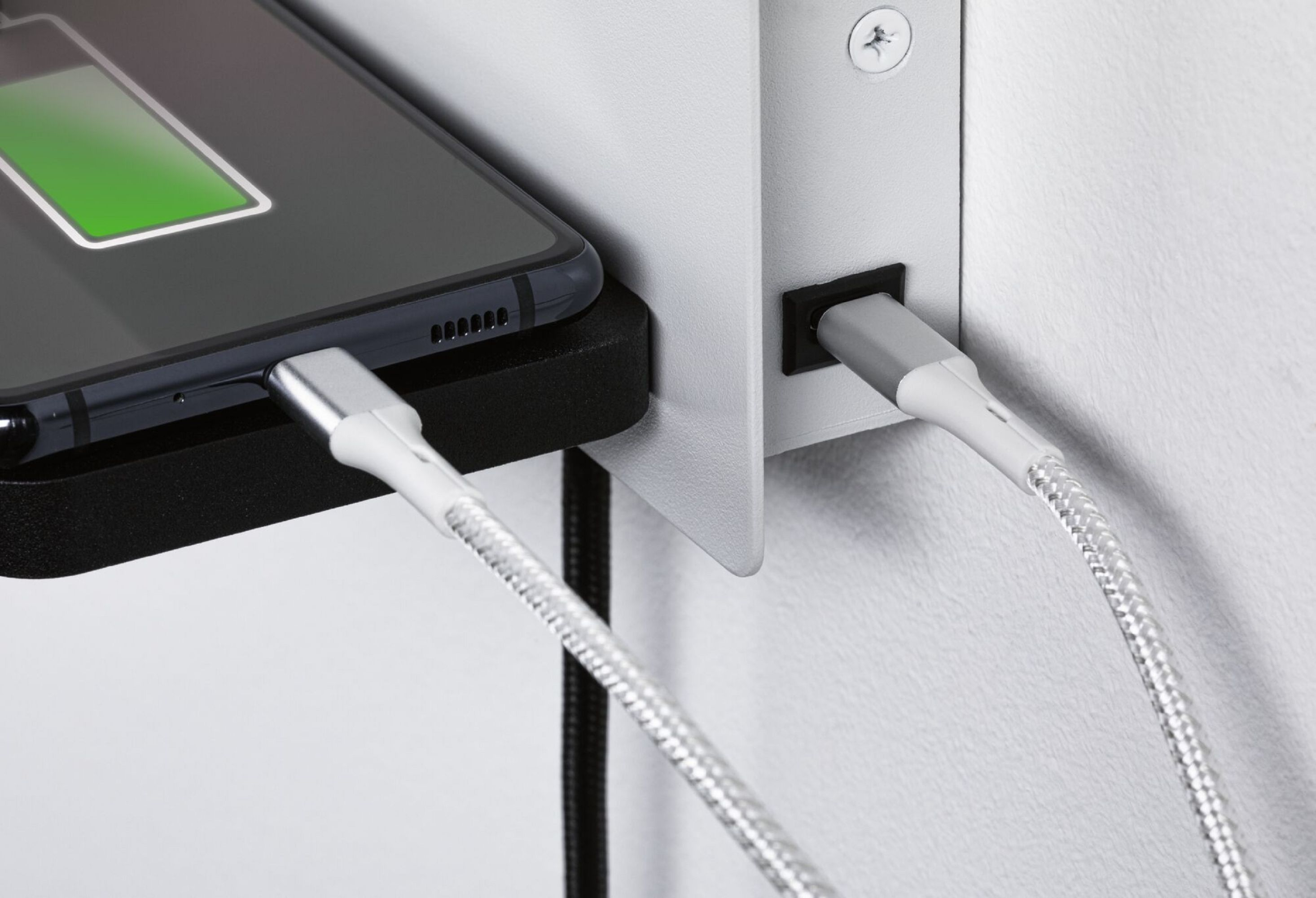 Telefon ładuje się z zieloną ikoną baterii. Biały kabel podłączony do telefonu i ściany.