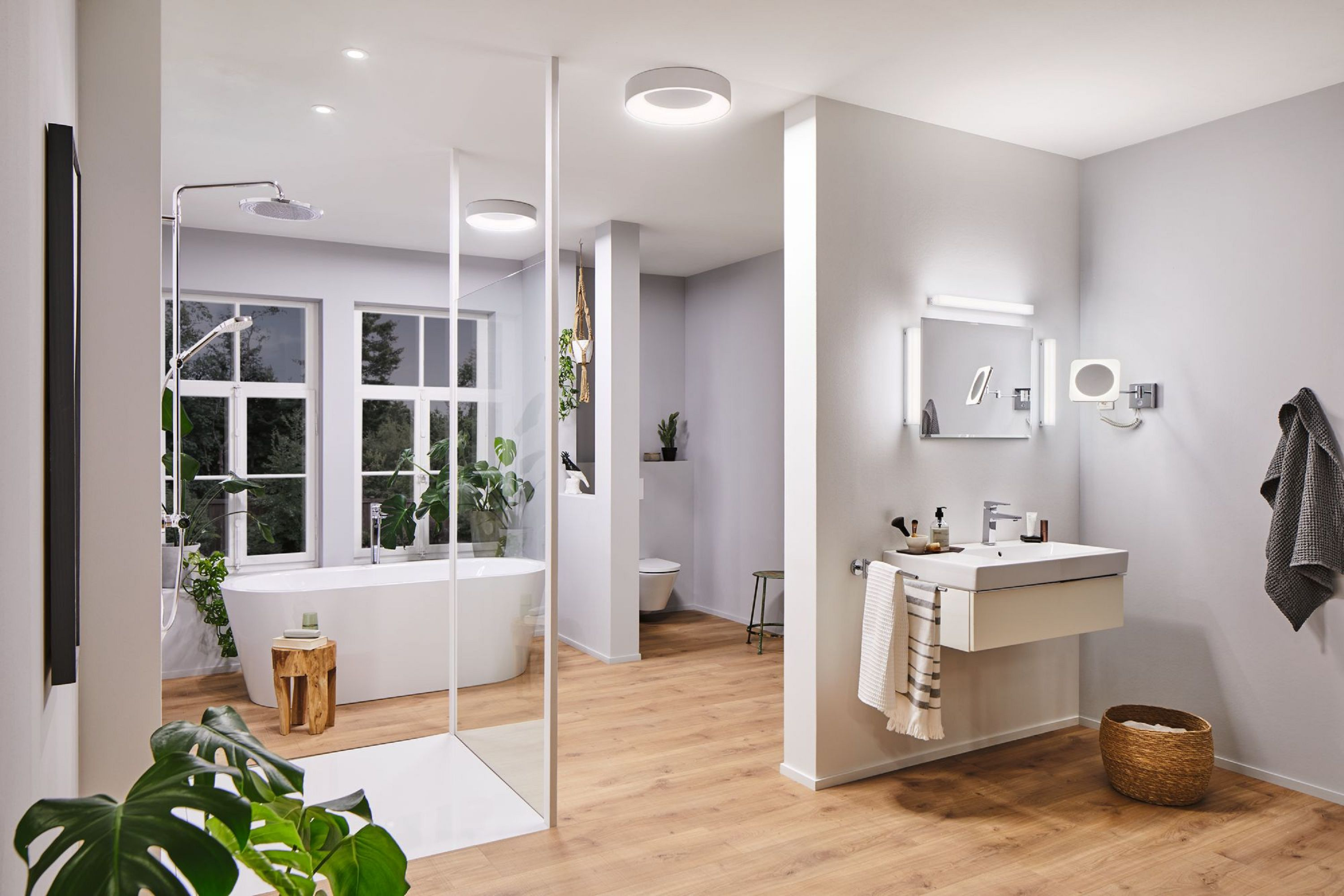 Nowoczesna łazienka z wanną, prysznicem, umywalką i toaletą. Rośliny i drewniana podłoga dodają naturalnego charakteru. Jasne oświetlenie.