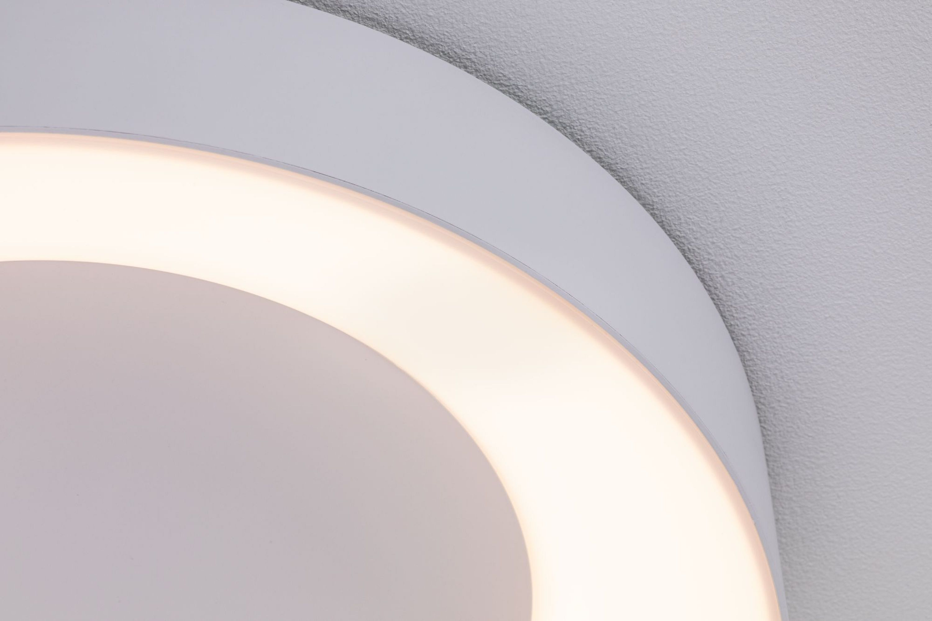 Gros plan d'un plafonnier blanc et circulaire avec une lumière chaude et brillante. L'arrière-plan est un mur gris texturé.