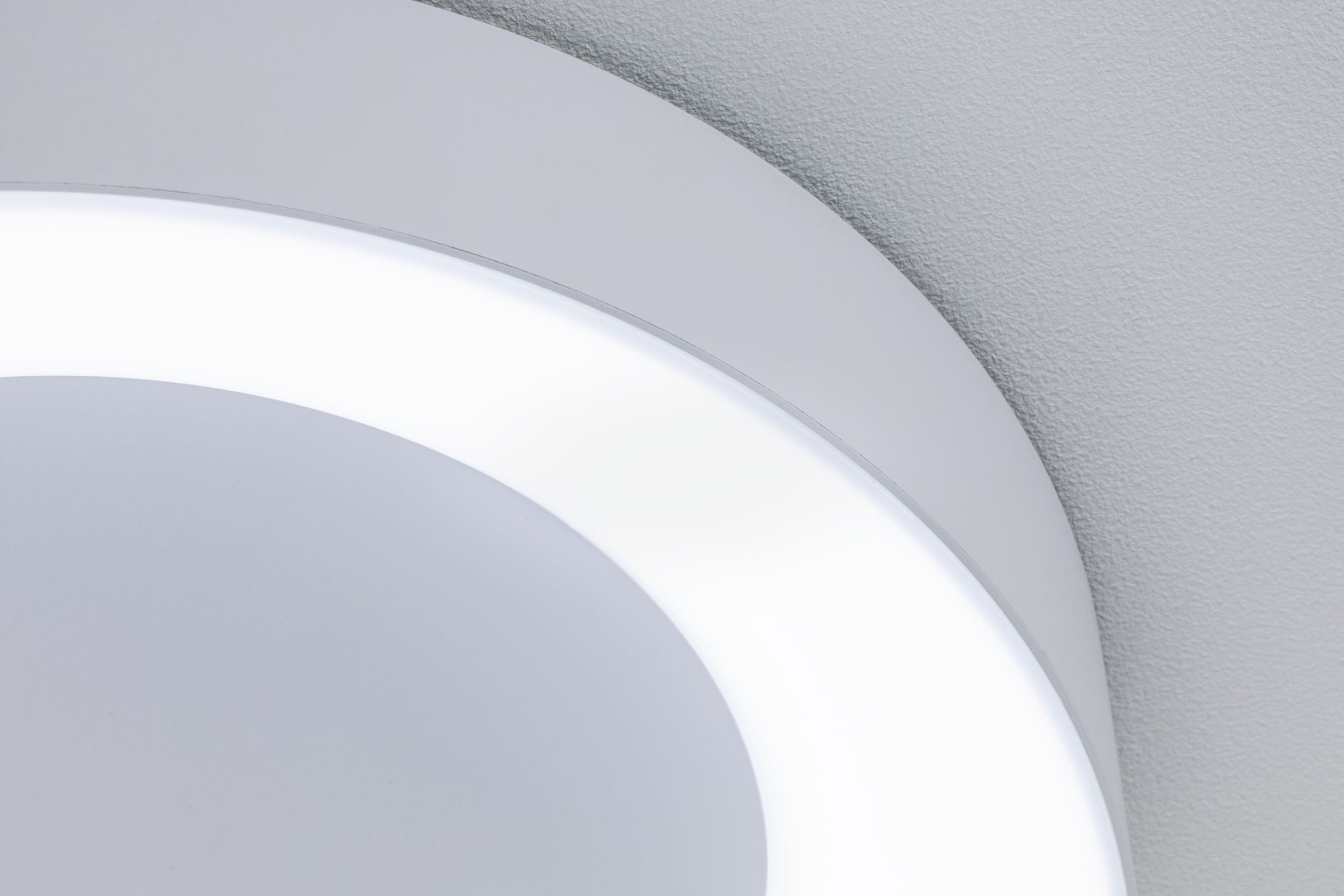 Gros plan d'un plafonnier LED blanc et circulaire avec une lueur vive. La lumière est montée sur un plafond gris texturé.
