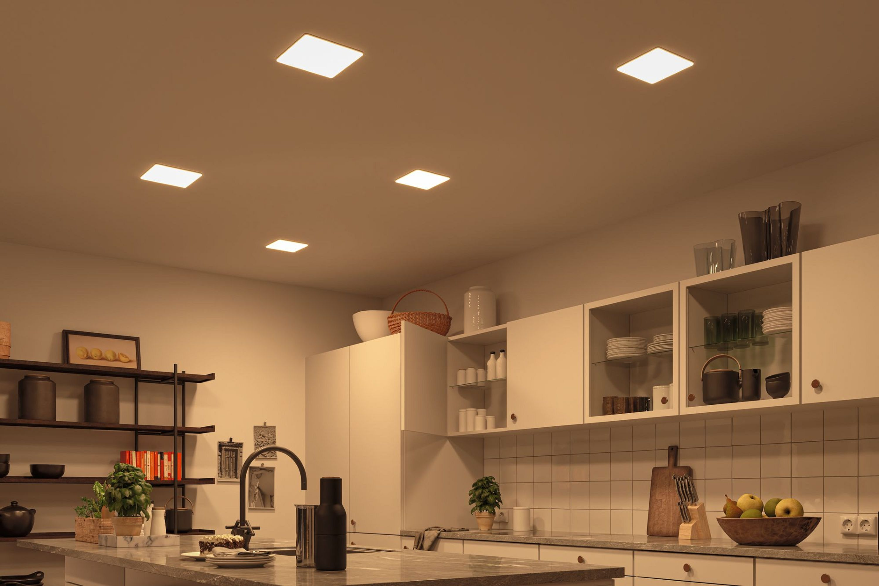 Una cucina con luminose luci a soffitto quadrate. Sono visibili armadi, scaffali e un piano di lavoro con oggetti. La scena è ben illuminata.