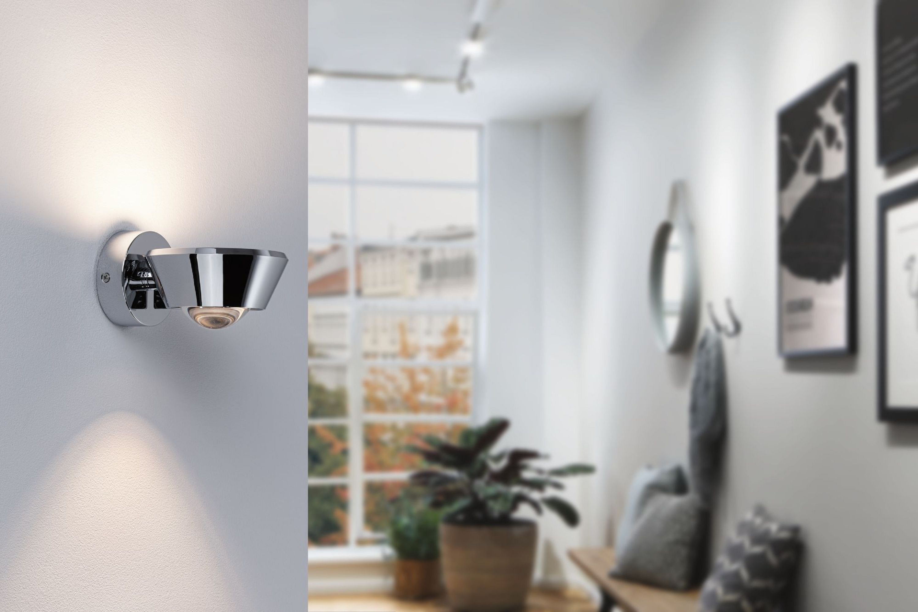 Ein moderner Flur mit einer Wandlampe, einem Fenster und einer Bank. Die Lampe strahlt Licht aus. Eine Pflanze und Bilder sind ebenfalls sichtbar.