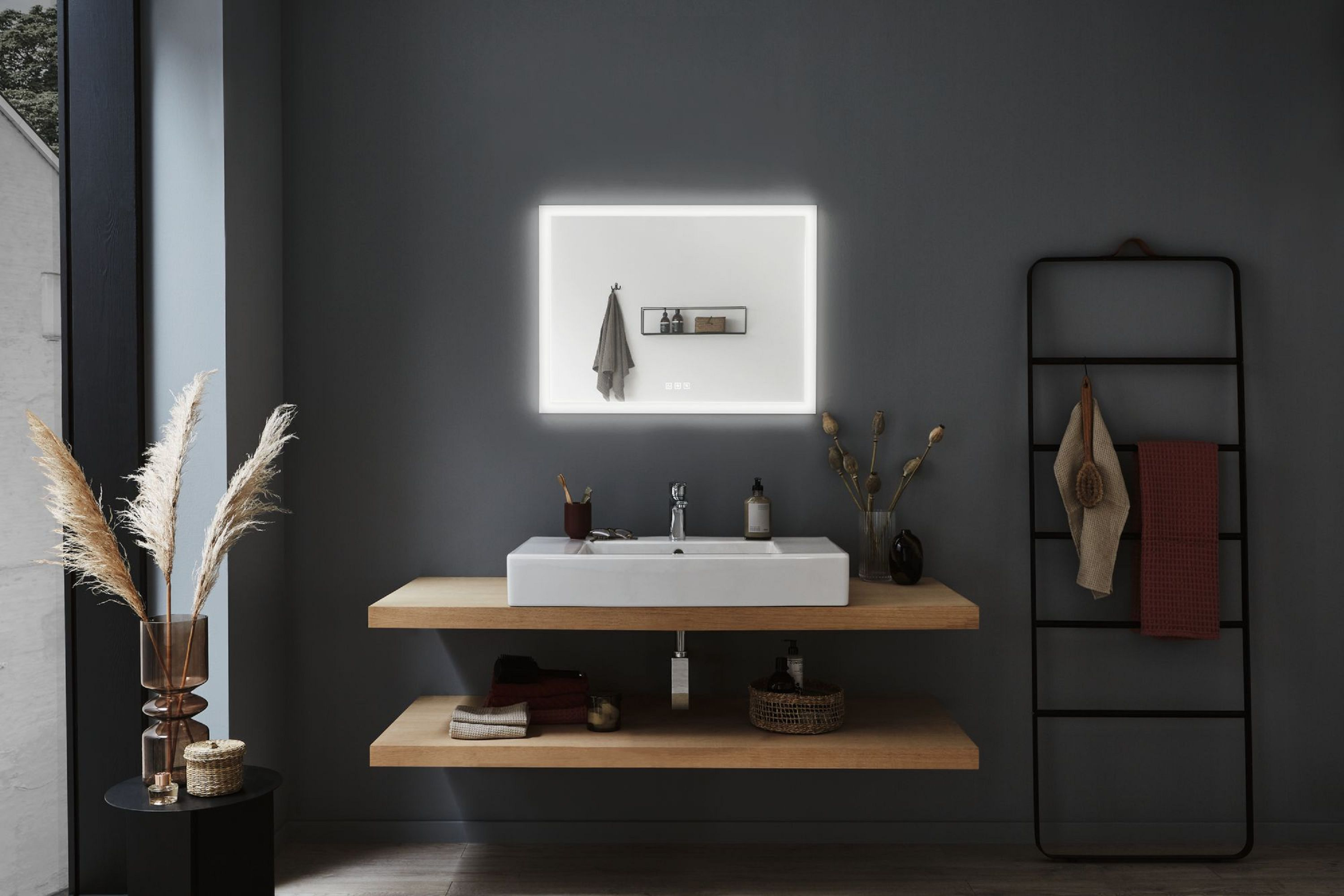 Badezimmer mit weißem Waschbecken, Spiegel und Holzregalen. Handtücher und Dekoration sind vorhanden. Die Wand ist dunkelgrau.