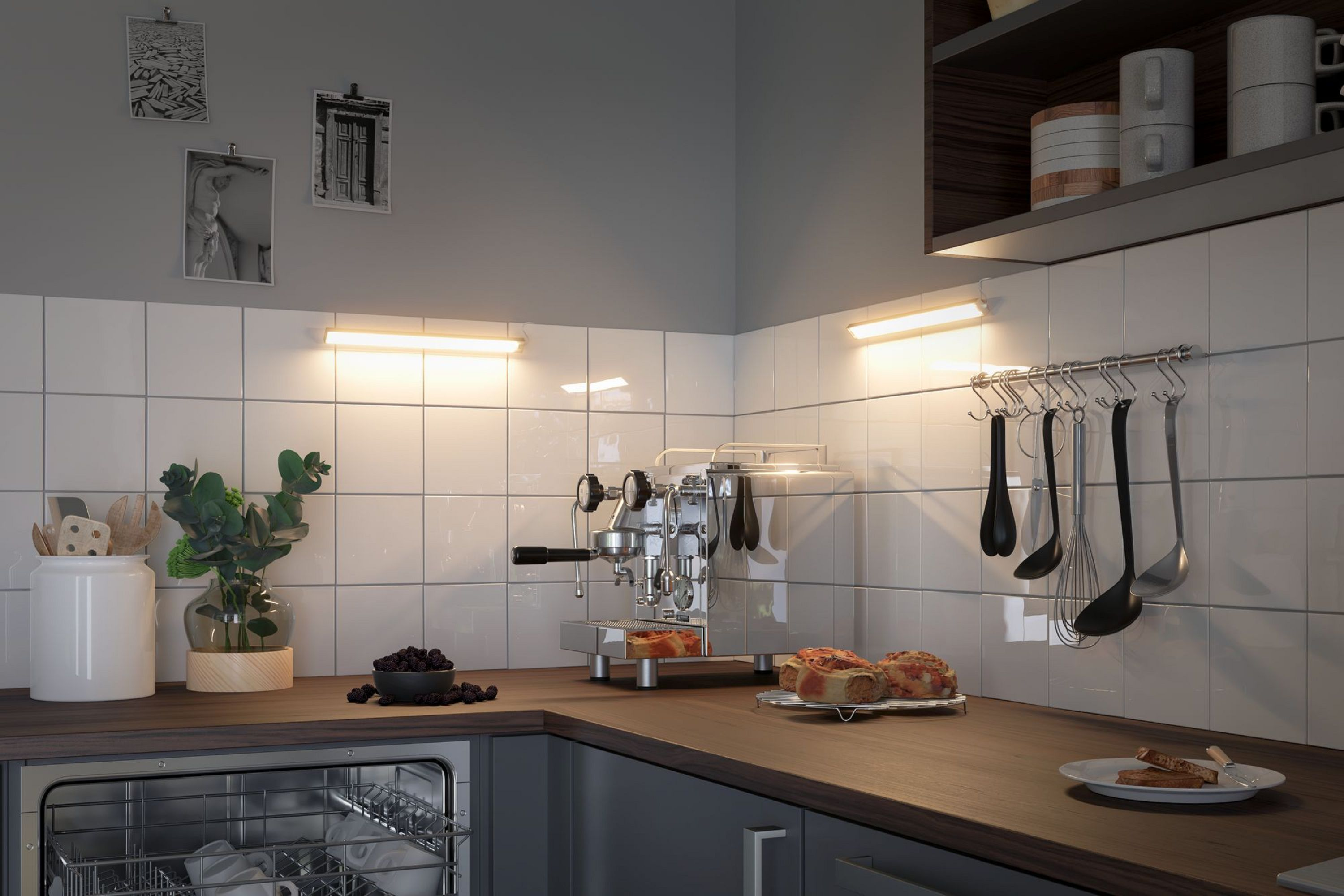 Küchenszene mit Kaffeemaschine, Gebäck und Utensilien. Weiße Fliesenwand, Holztheke. Bilder an der Wand, und Geschirrspüler ist sichtbar.