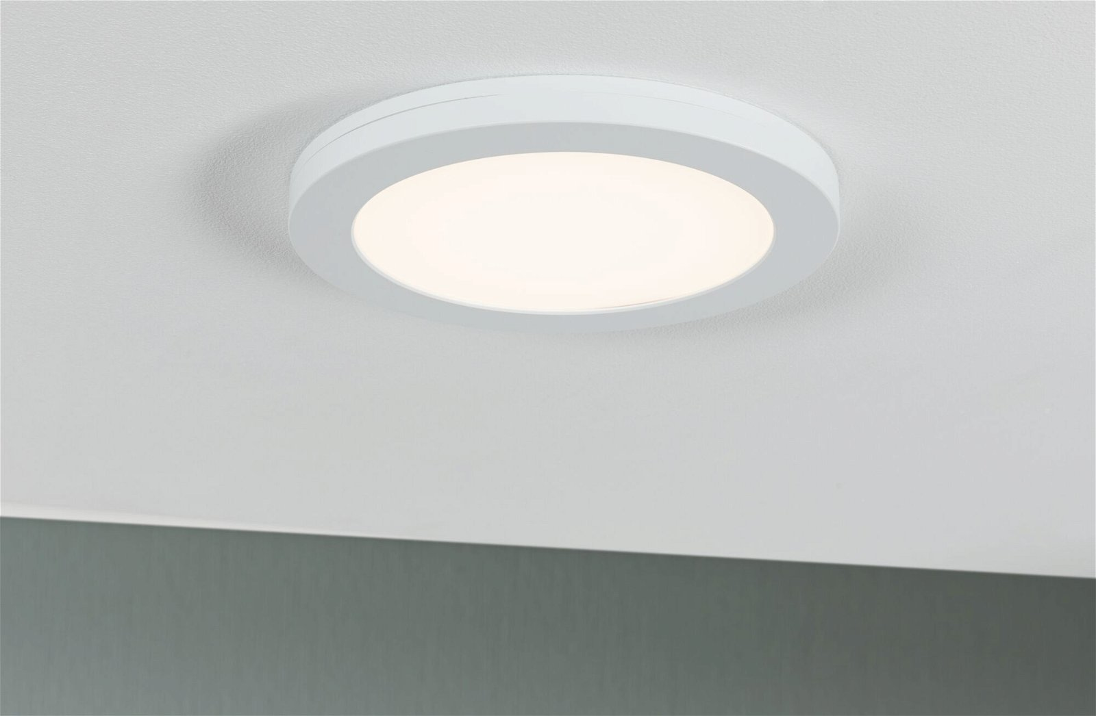 Biała, okrągła lampa sufitowa jest wyśrodkowana na białym suficie. Światło emituje delikatną poświatę.