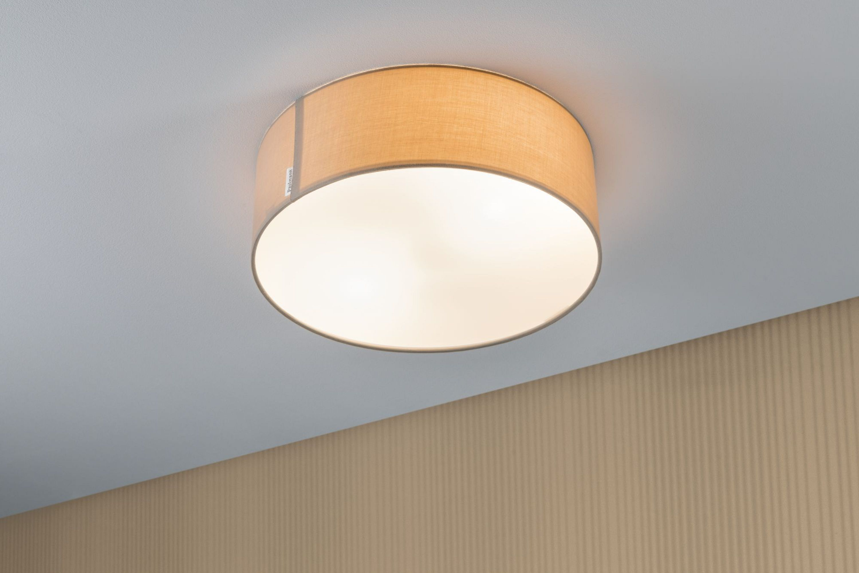 Lampa sufitowa z beżowym kloszem i białym wnętrzem jest zamontowana na białym suficie.