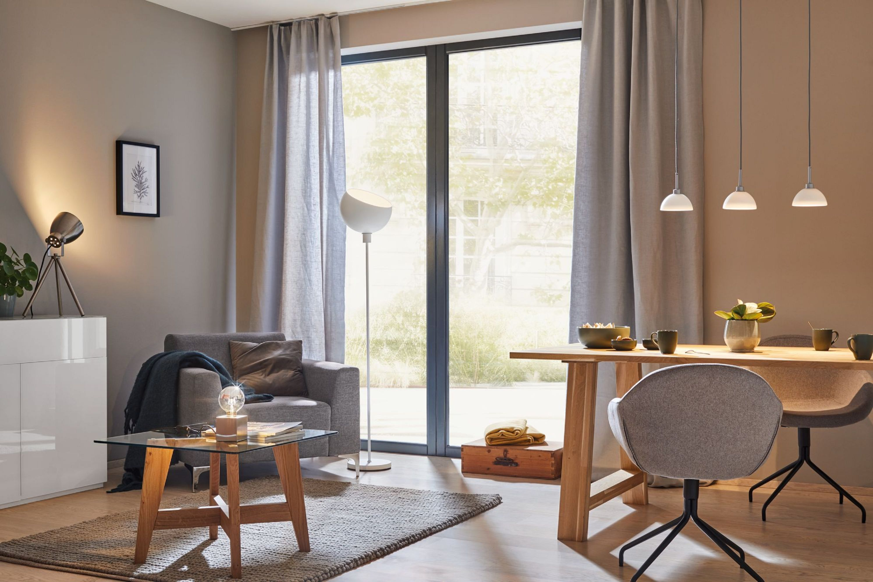 Salon z szarymi zasłonami, sofą, stołem i oknem z widokiem na ogród. Wiszące lampy.