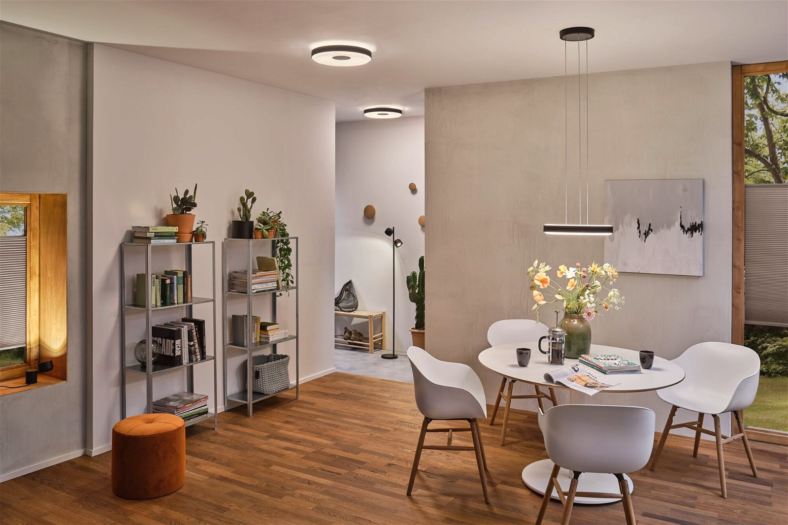 Scena we wnętrzu z stołem jadalnym, krzesłami, regałami i roślinami. Nowoczesna, dobrze oświetlona przestrzeń mieszkalna z drewnianymi podłogami.