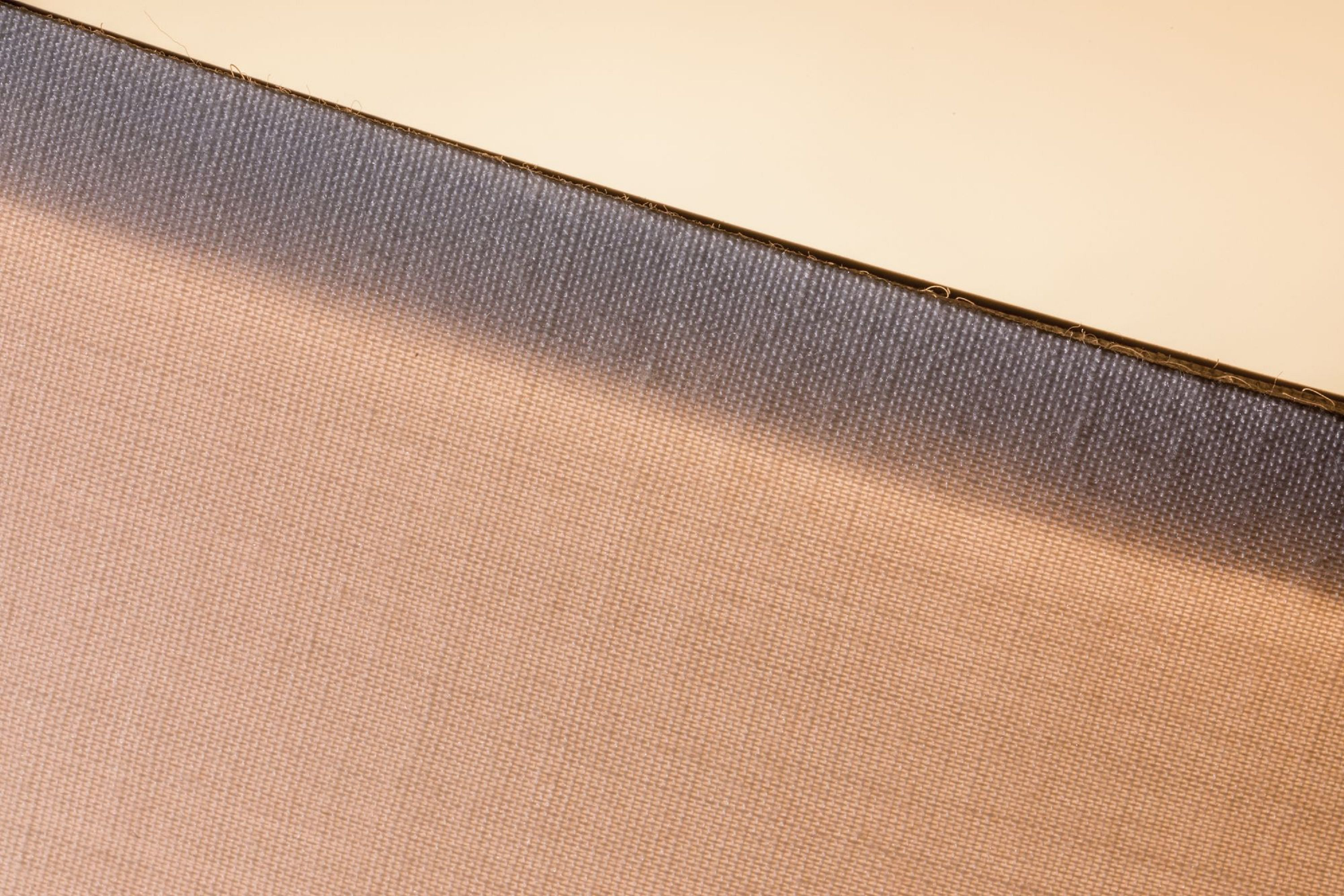 Zbliżenie na teksturowaną tkaninę w odcieniach beżu i szarości, z przekątną linią dzielącą kolory. Góra jest jasnobeżowa.