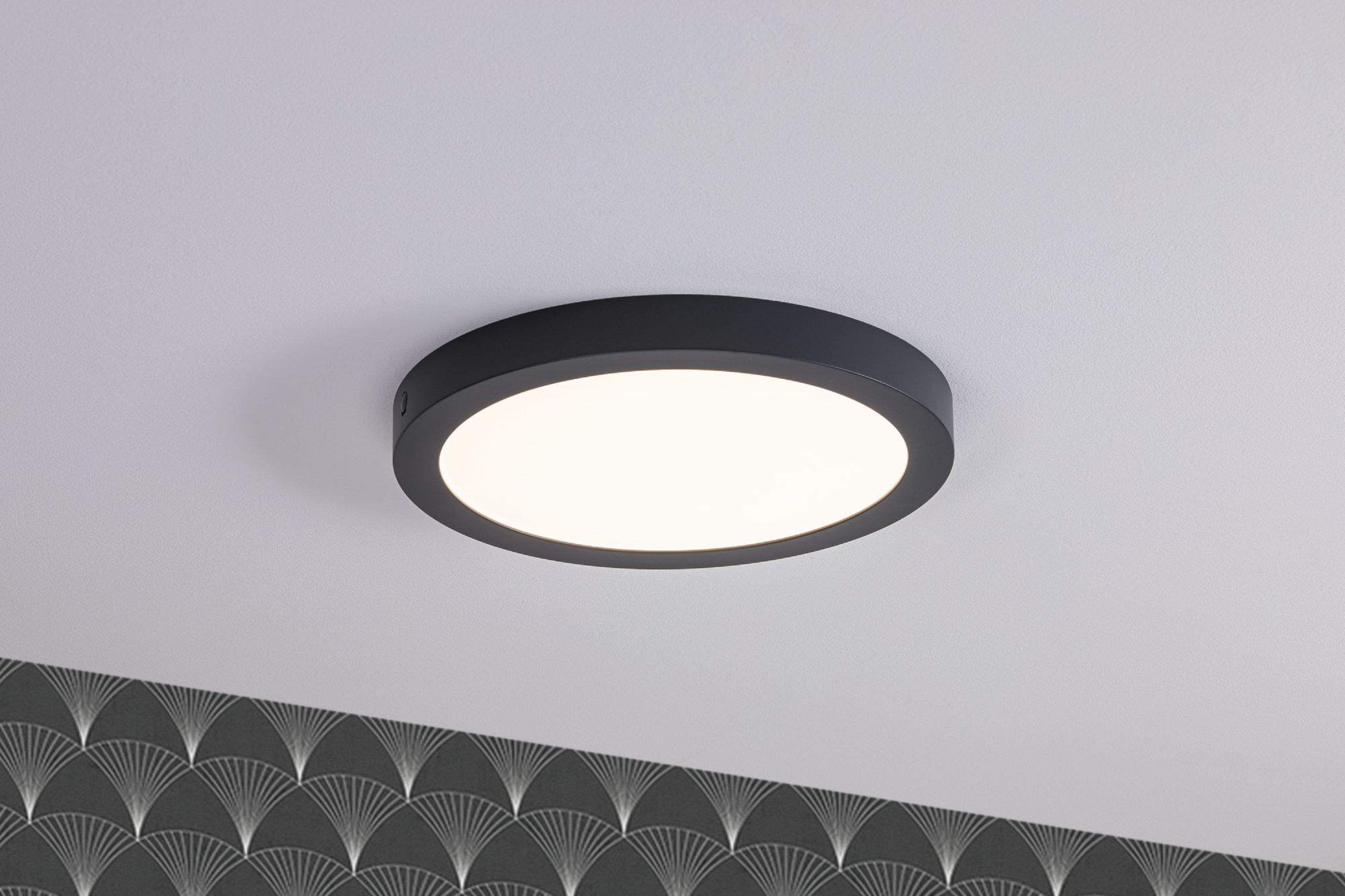 Una plafoniera rotonda nera con un centro bianco brillante. Sotto, una carta da parati grigio scuro è visibile.