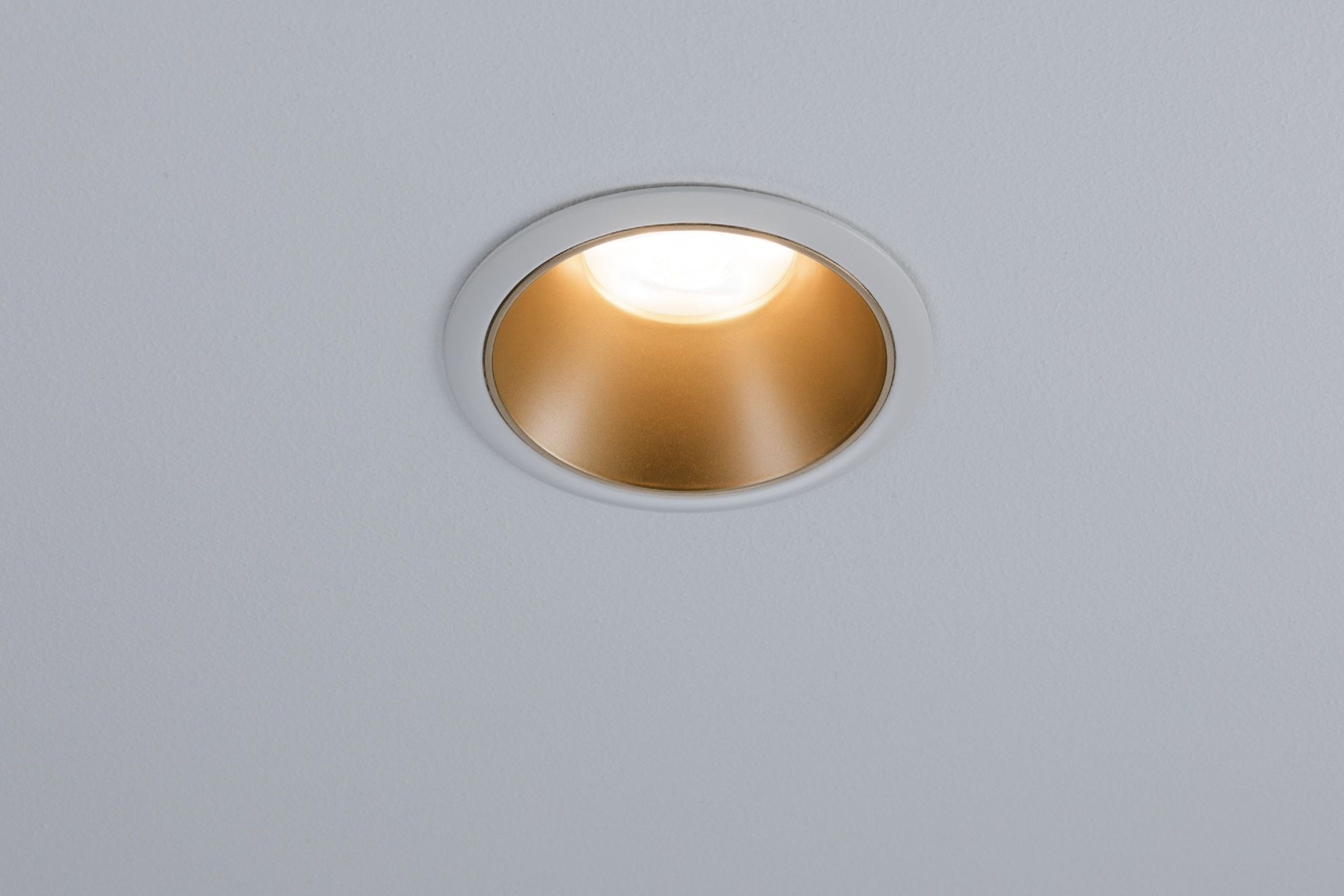 Un faretto da incasso. Ha un anello esterno bianco e l'interno dorato. La luce è accesa.