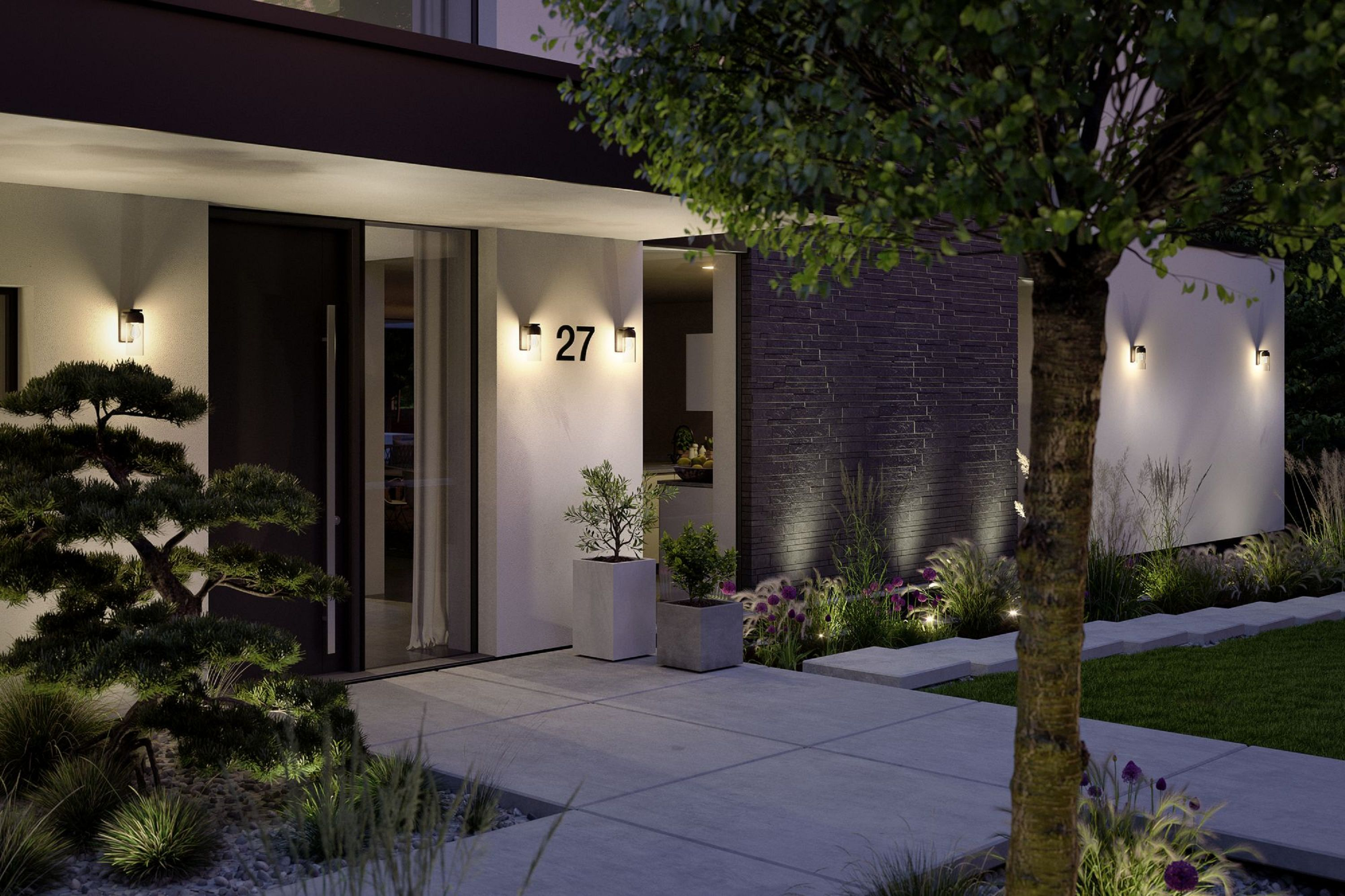 Widok zewnętrzny nowoczesnego domu o zmierzchu. Oświetlona ścieżka, rośliny i drzewo z przodu. Widoczny numer domu 27.