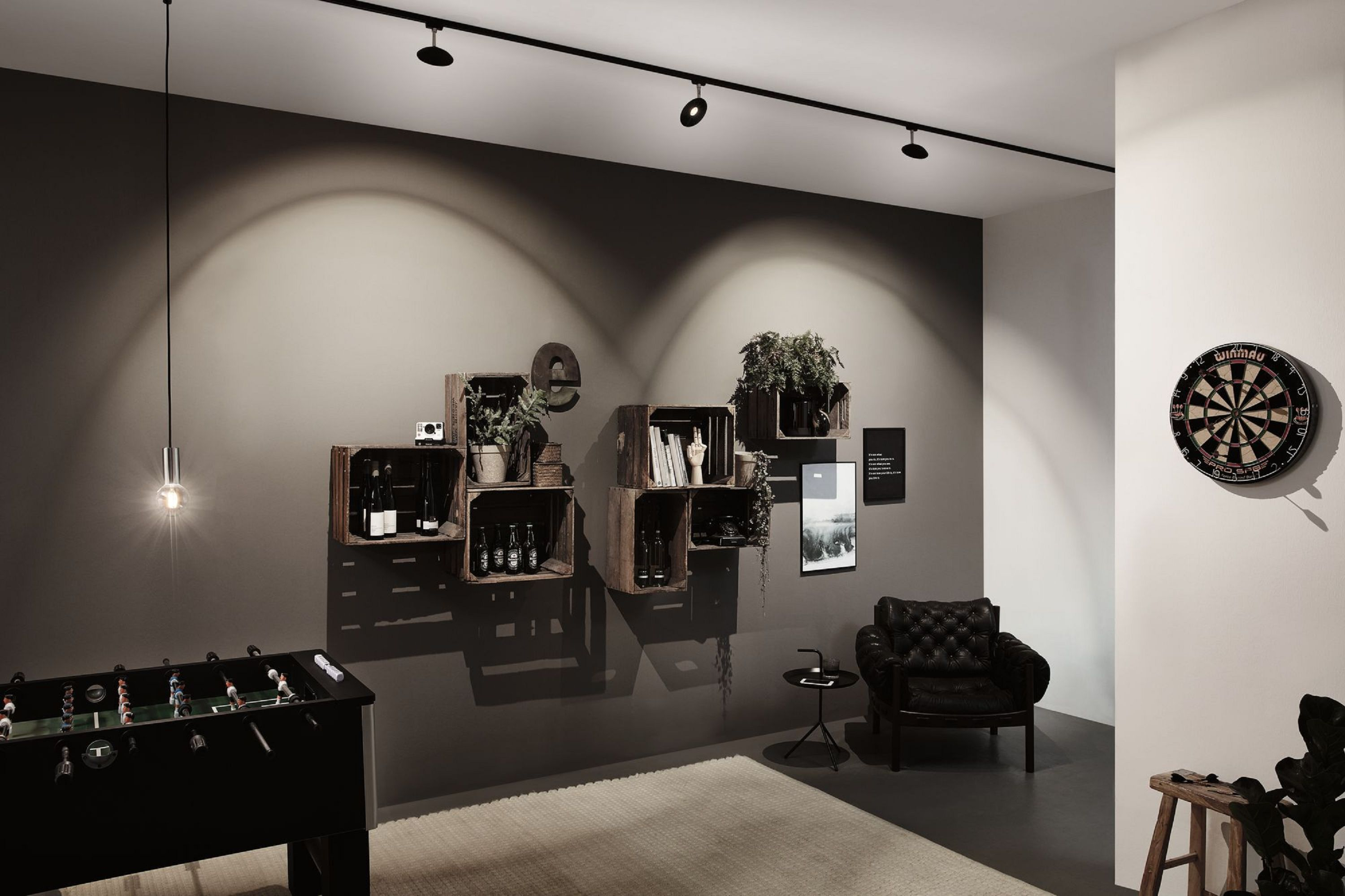 Pokój z piłkarzykami, drewnianymi skrzyniami na ścianie, tarczą do darta, skórzanym fotelem i dywanem.