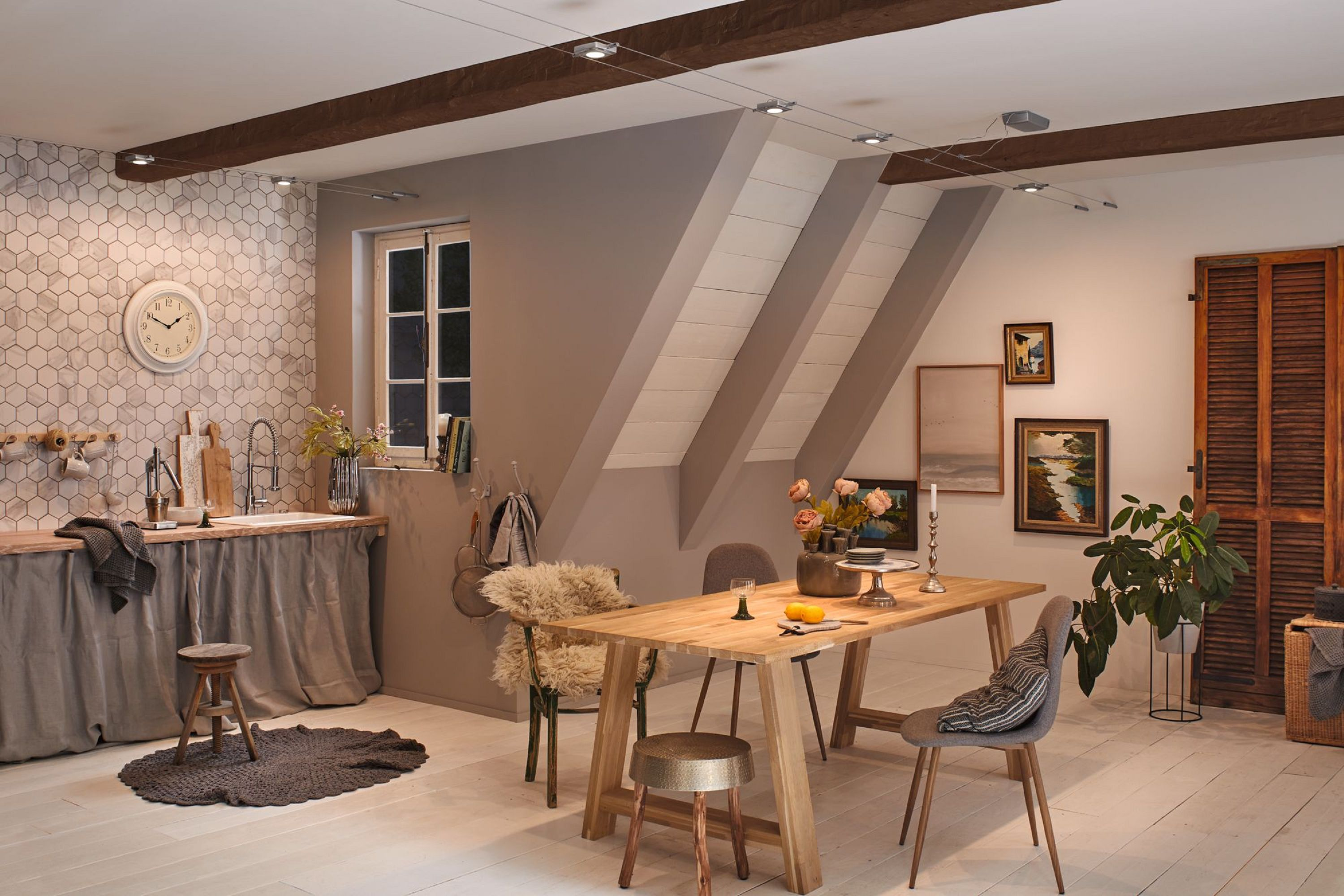 Scatto interno di una zona pranzo con tavolo in legno, sedie e opere d'arte alle pareti. Cucina visibile.