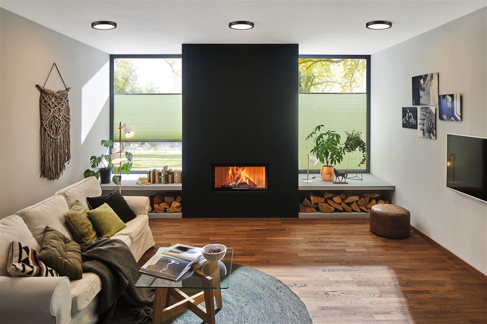 Nowoczesny salon z kominkiem, sofą i dużymi oknami z zielonymi żaluzjami. Drewniana podłoga i dywan.