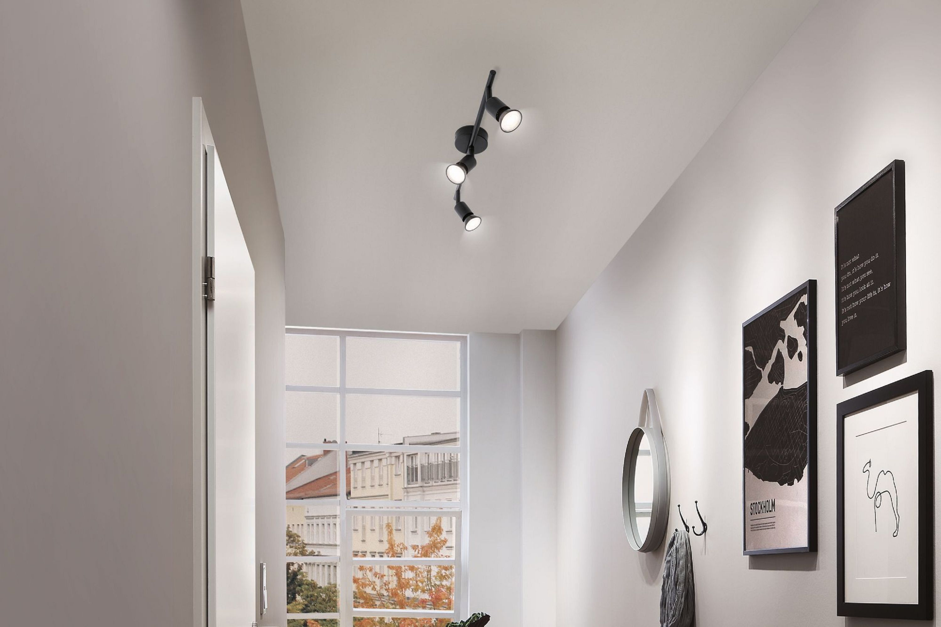 Flur mit Schienenbeleuchtung, Spiegel, Kunst und Fenster. Blick auf die Stadt. Weiße Wände und Decke.