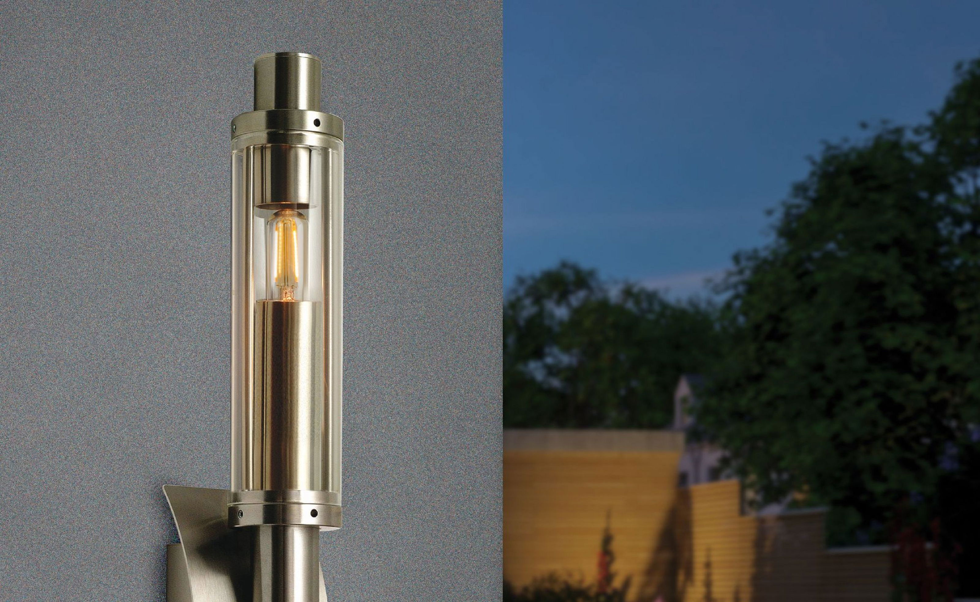 Eine moderne Außenlampe mit einer leuchtenden Glühbirne, vor einem dunkelblauen Himmel und verschwommenem Garten.