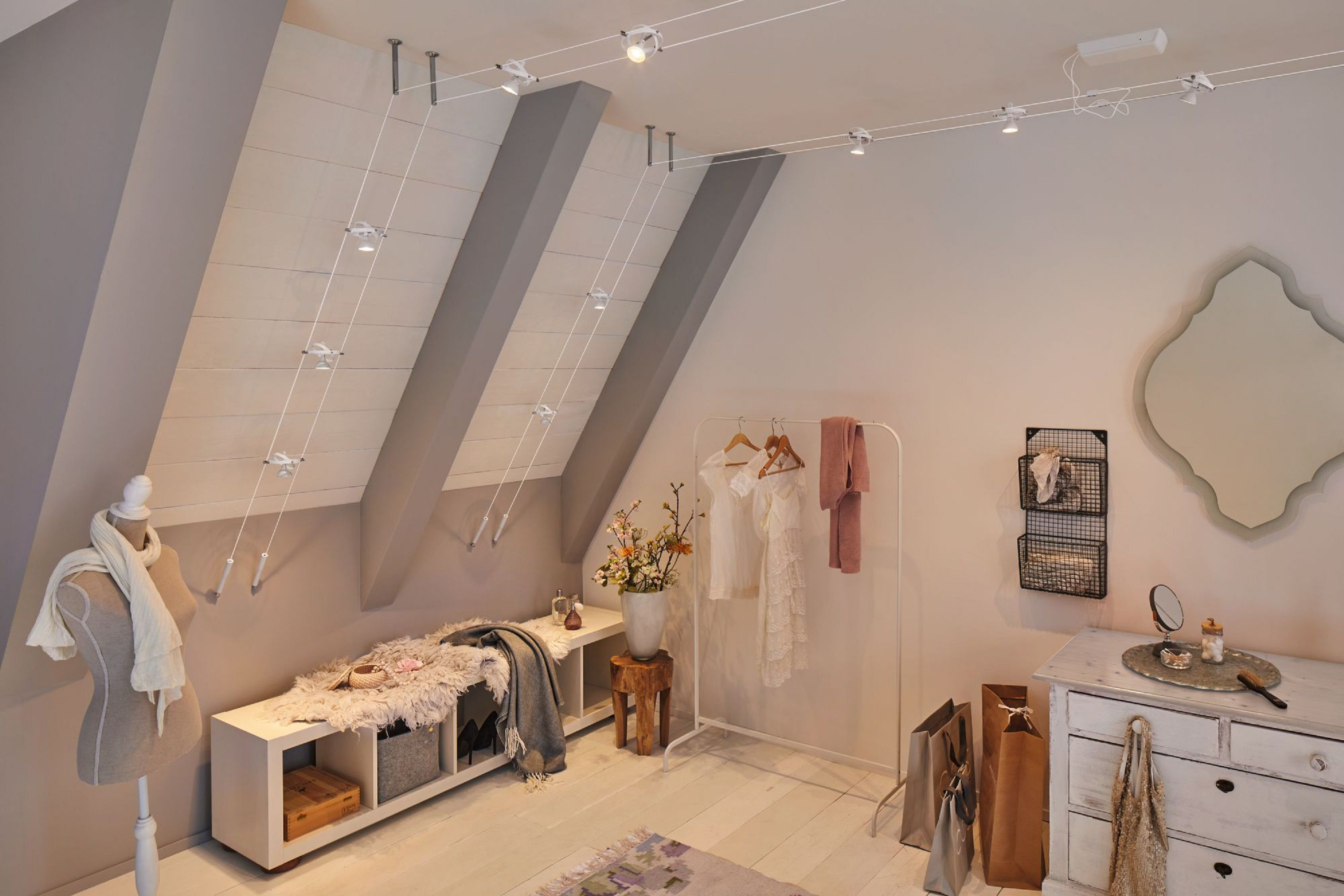 Una stanza con soffitto spiovente, luci, attaccapanni, manichino, cassettiera e specchio.