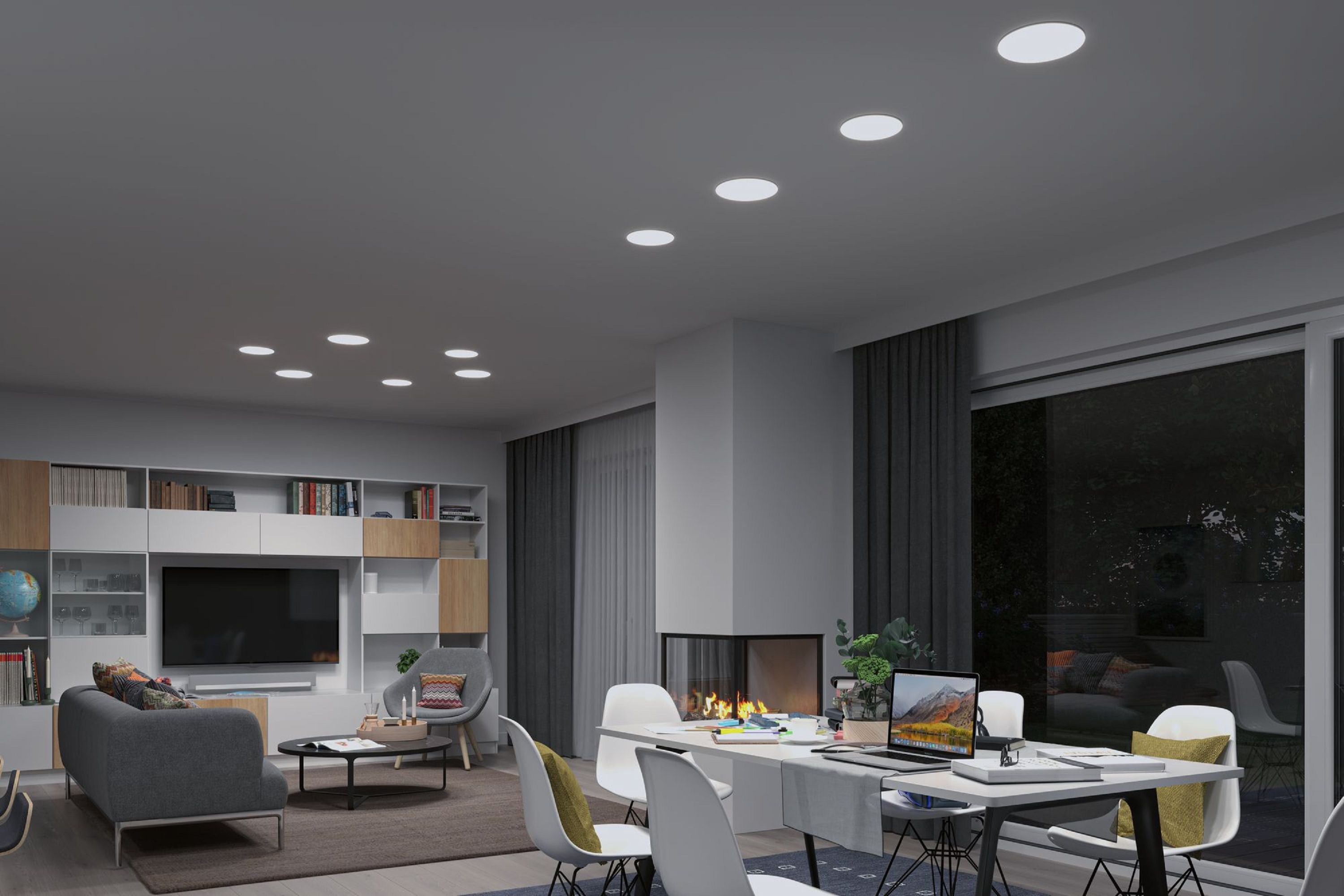 Soggiorno moderno con camino, tavolo da pranzo e divano. Luci a soffitto luminose. Grandi finestre si affacciano su una scena notturna buia.