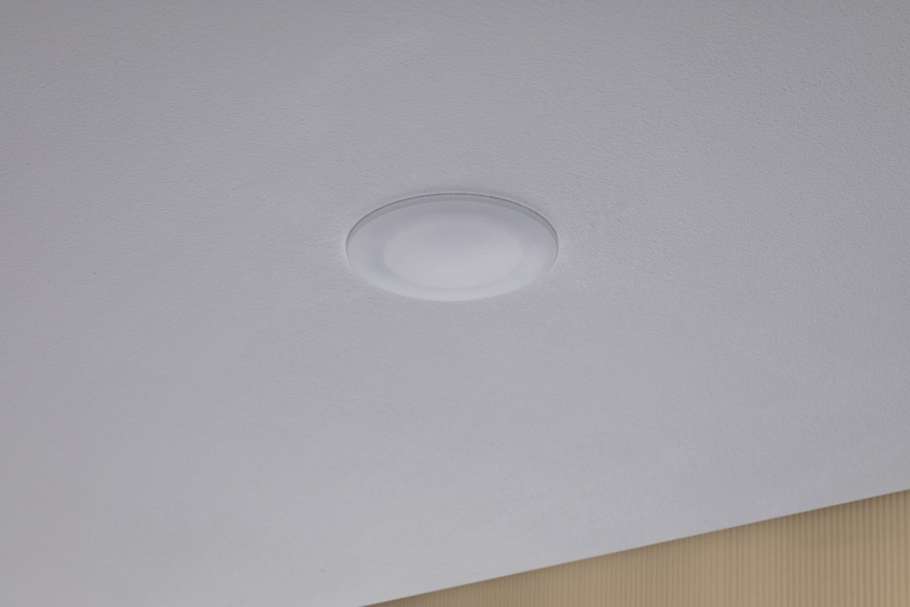 Un soffitto con un apparecchio di illuminazione circolare. Il soffitto è bianco. È visibile una sezione di muro beige.