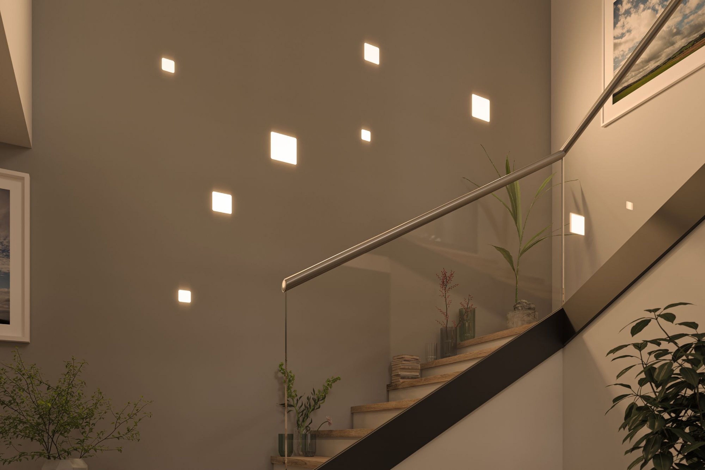 Una scala con luci quadrate sulla parete. Sono presenti piante e un parapetto in vetro. Ci sono quadri sul muro.