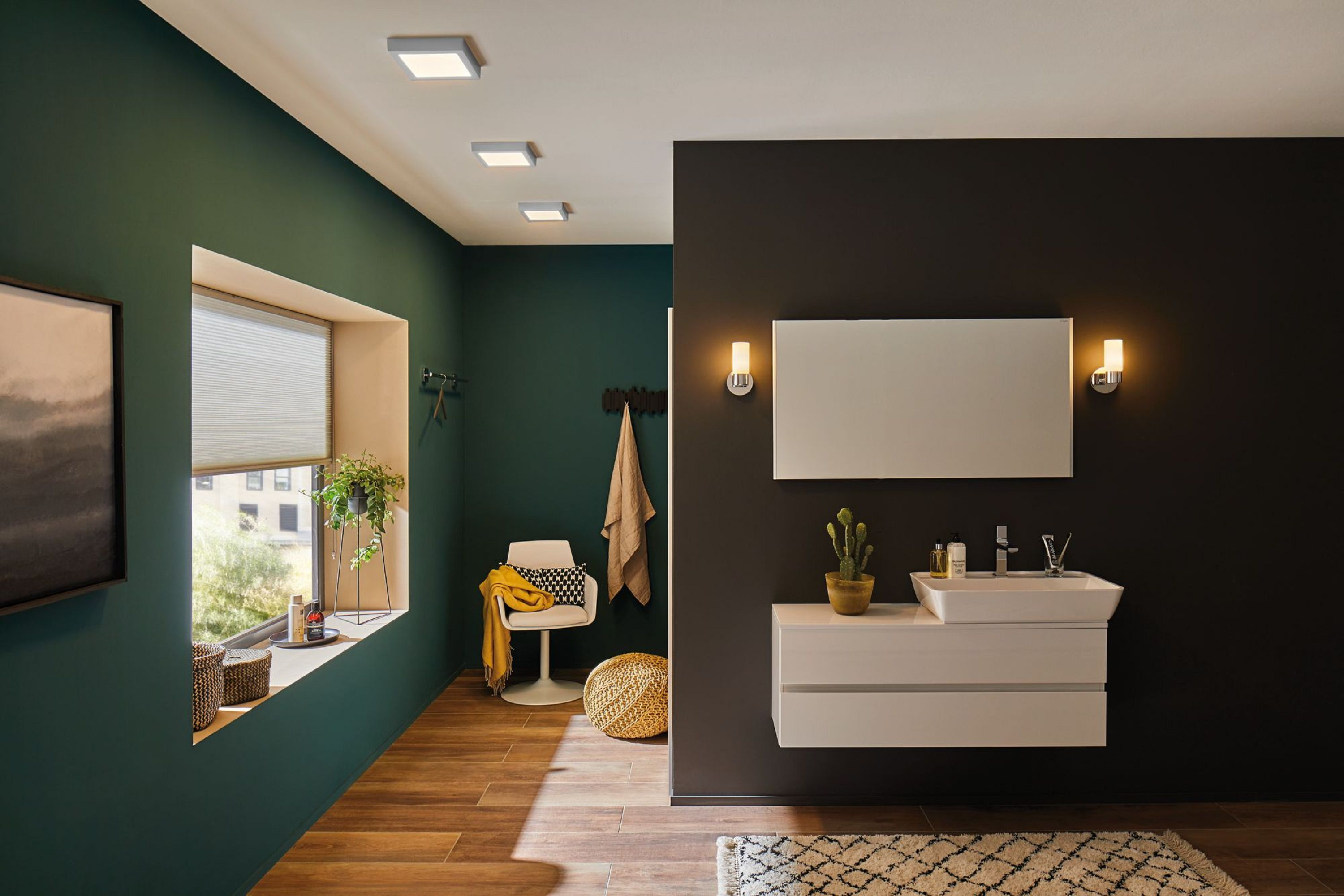 Bagno moderno con pareti verde scuro e nere, un mobile lavabo bianco e pavimento in legno. Include una finestra e una sedia.
